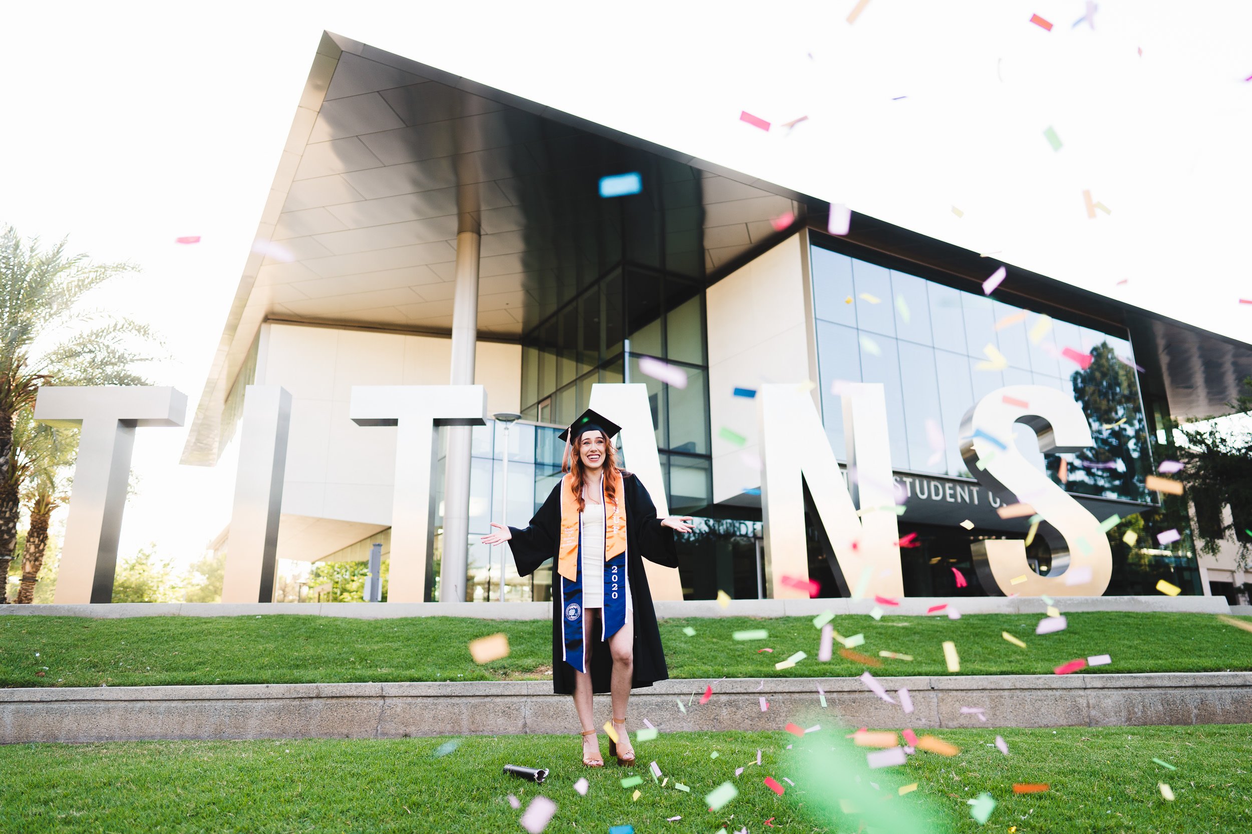 CSUF Graduation Portrait in front of Titans Sign with confetti, CSU Fullerton graduate.