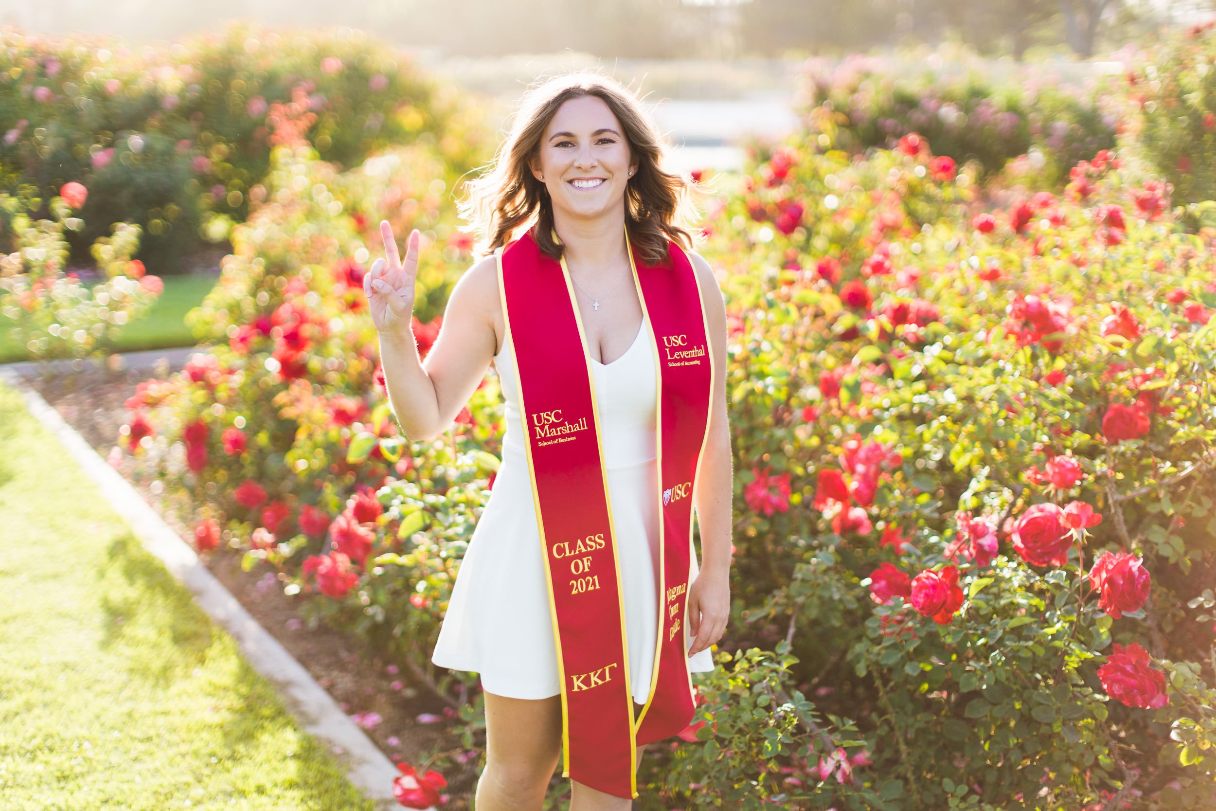 USC Rose Garden Graduation Portraits of graduate with sash giving Victory sign.