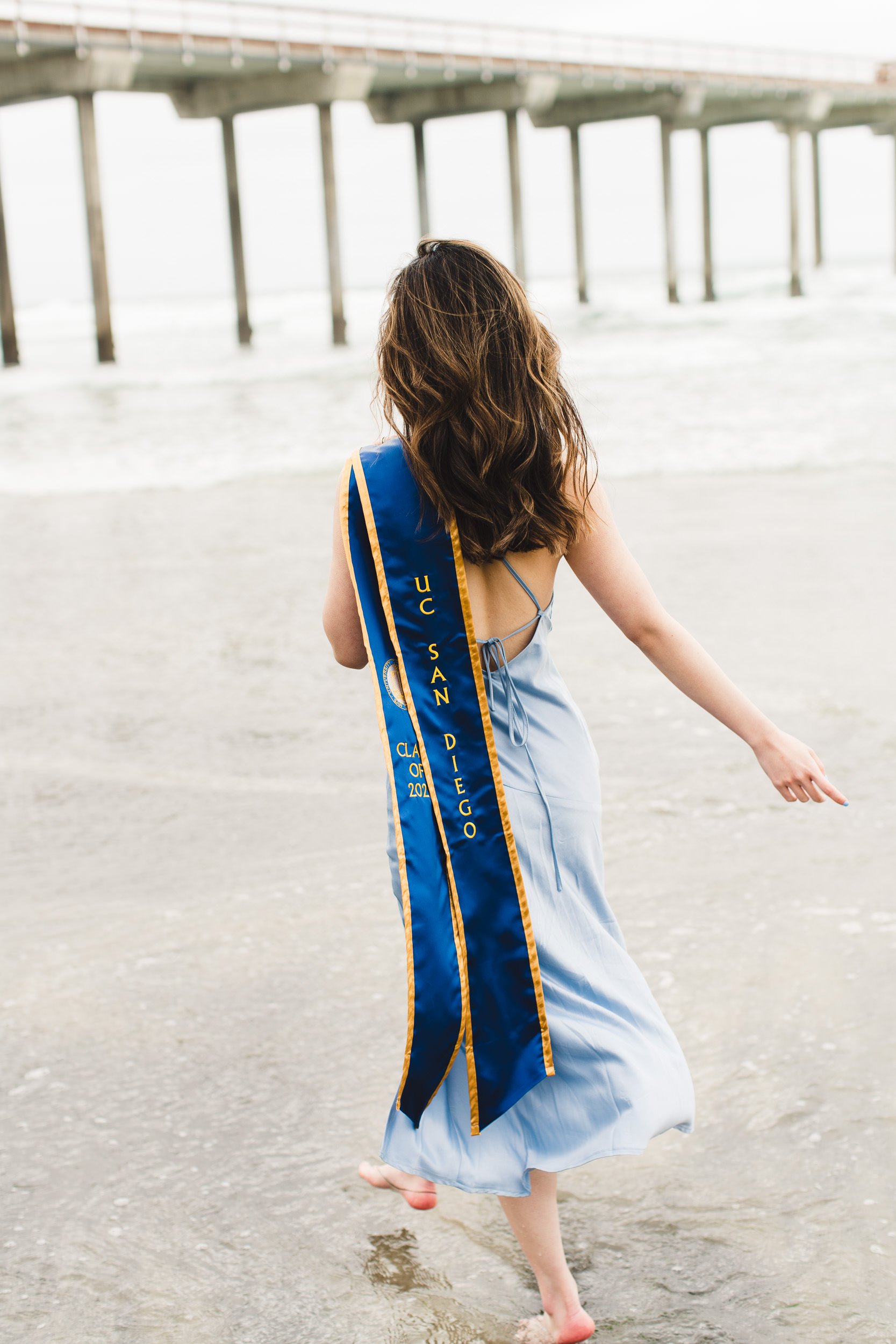 Dreamy graduation portraits at beach, grad sash over shoulder walking in the water. Los Angeles, CA