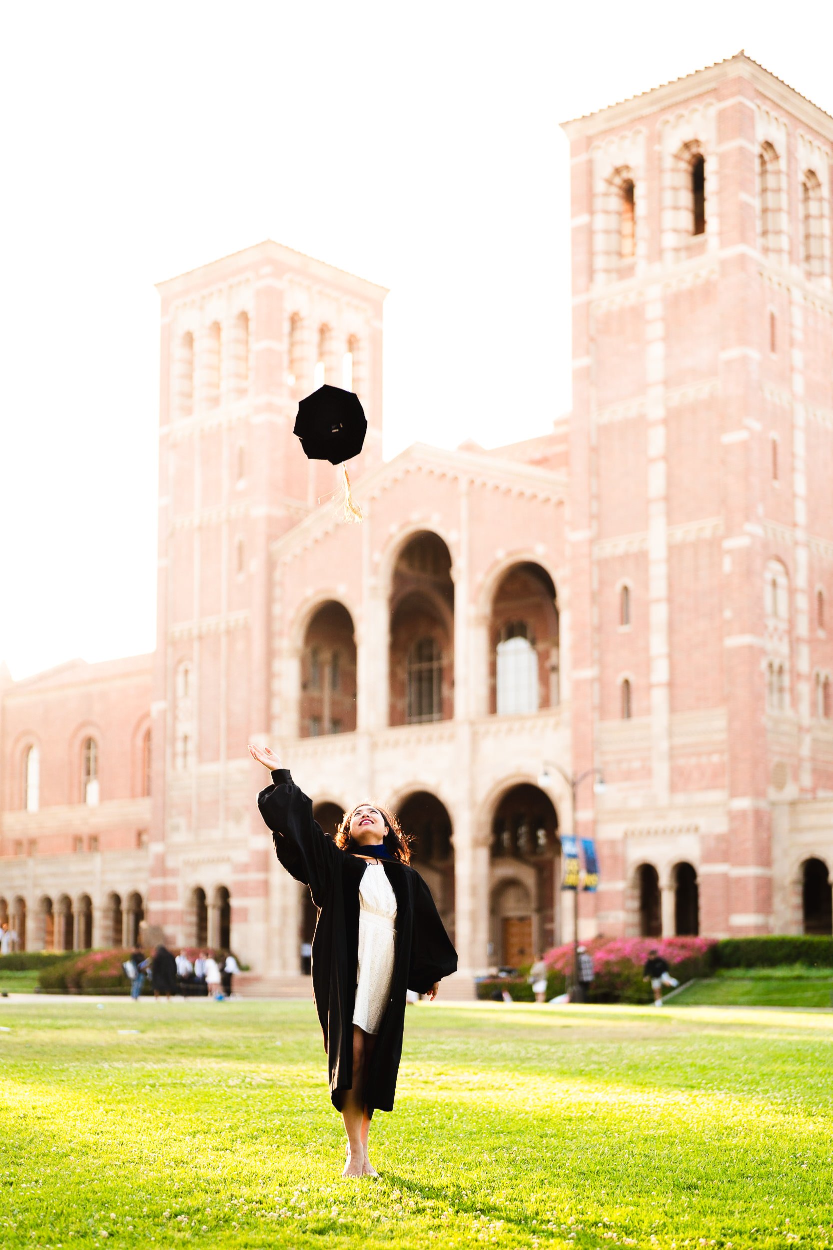 UCLA Doctorate Graduate tossing cap at Royce Hall at sunset