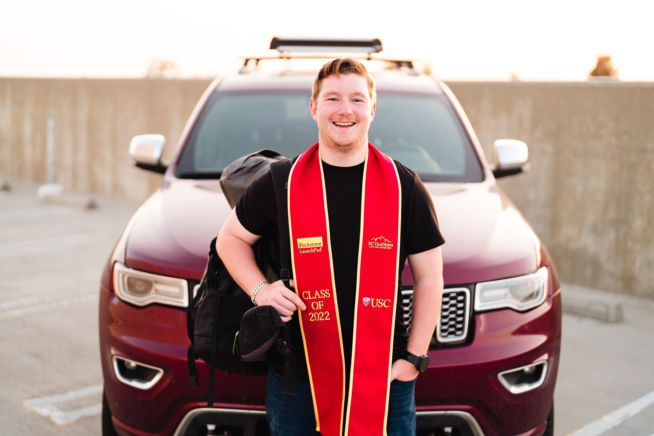 Graduation portrait on rooftop garage at sunset with cars