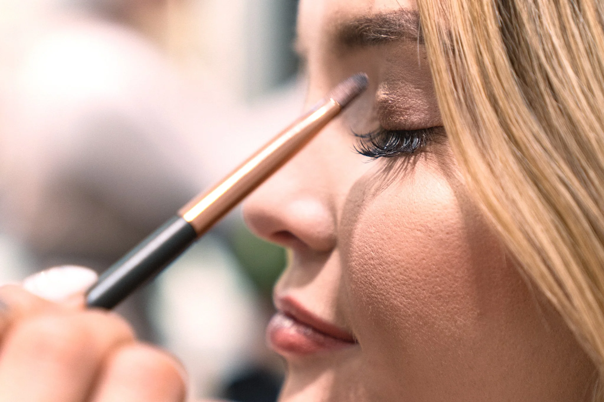 Close-up of makeup brush applying warm eyeshadow to model's eyelid – precision and artistry at a Calgary beauty boutique event. Detailed glamour captured by Stance Creative.