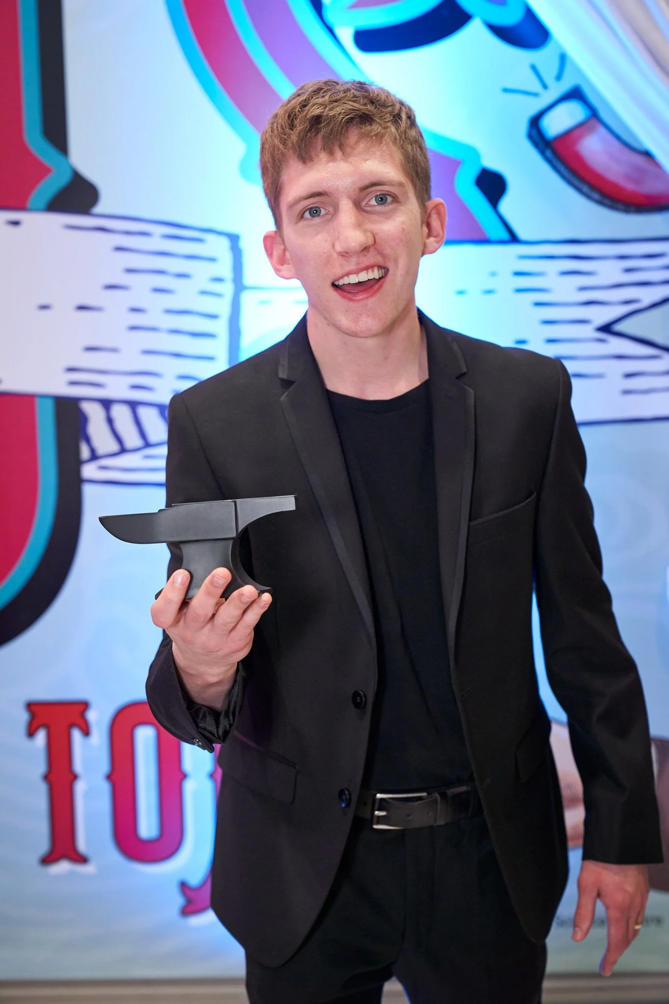 Anvil award winner proudly showing off his new hardware at the Telus Spark – beaming smile against colorful backdrop. Exciting moment captured by Stance Creative, professional Calgary event photographer.