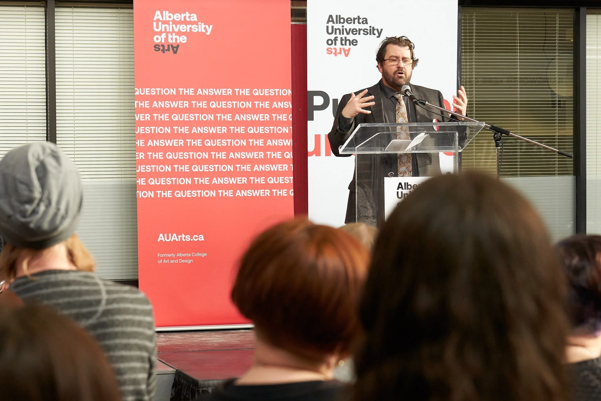 Daniel Doz at the podium during AUArts (Alberta University of the Arts) event in Calgary – passionate delivery under bold red banners. Inspiring academic moment captured by Stance Creative.