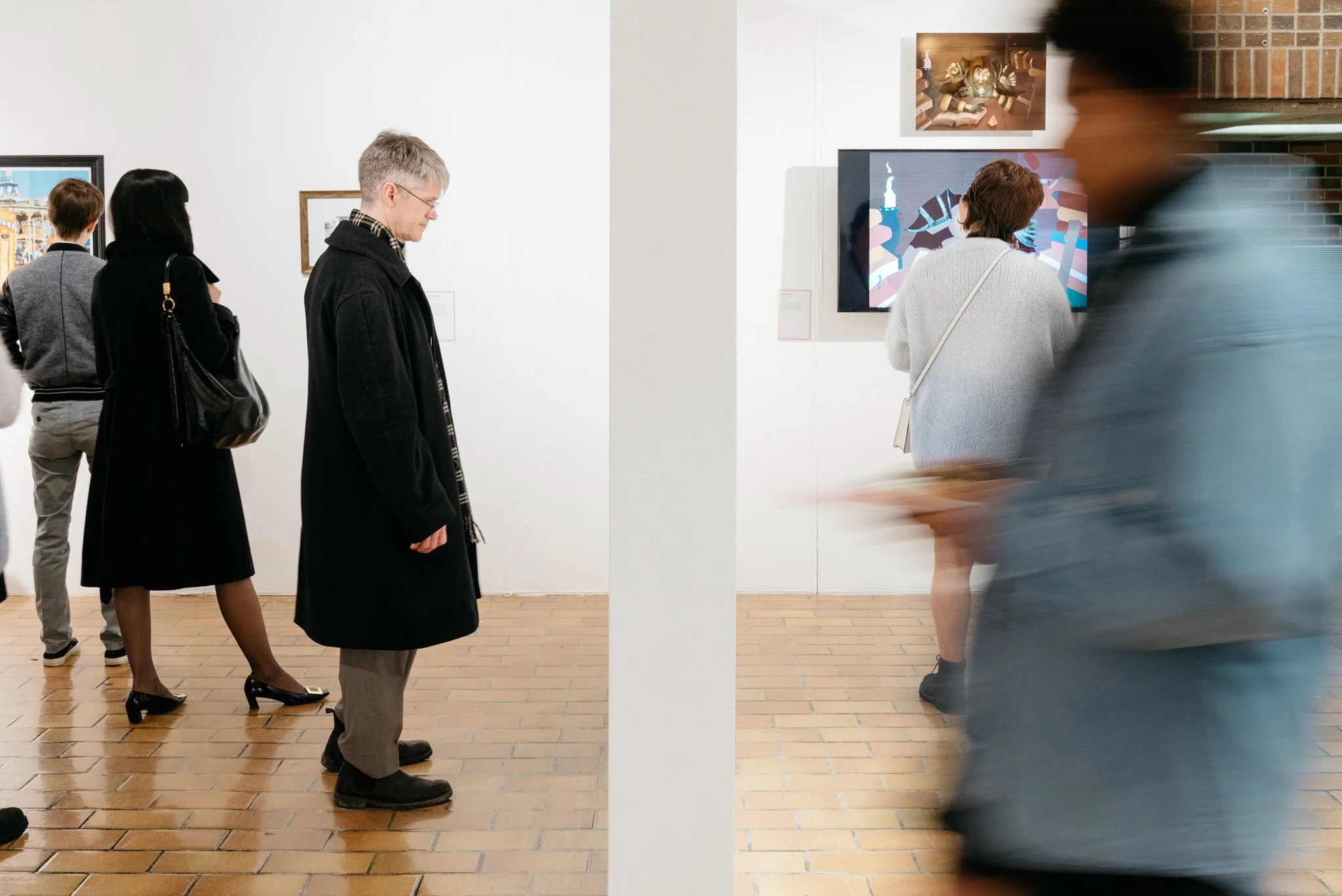 Attendees exploring AU Arts Student Showoff art gallery – blurred figures in motion admiring framed portraits and modern pieces on white walls. Dynamic cultural scene photographed by Stance Creative.