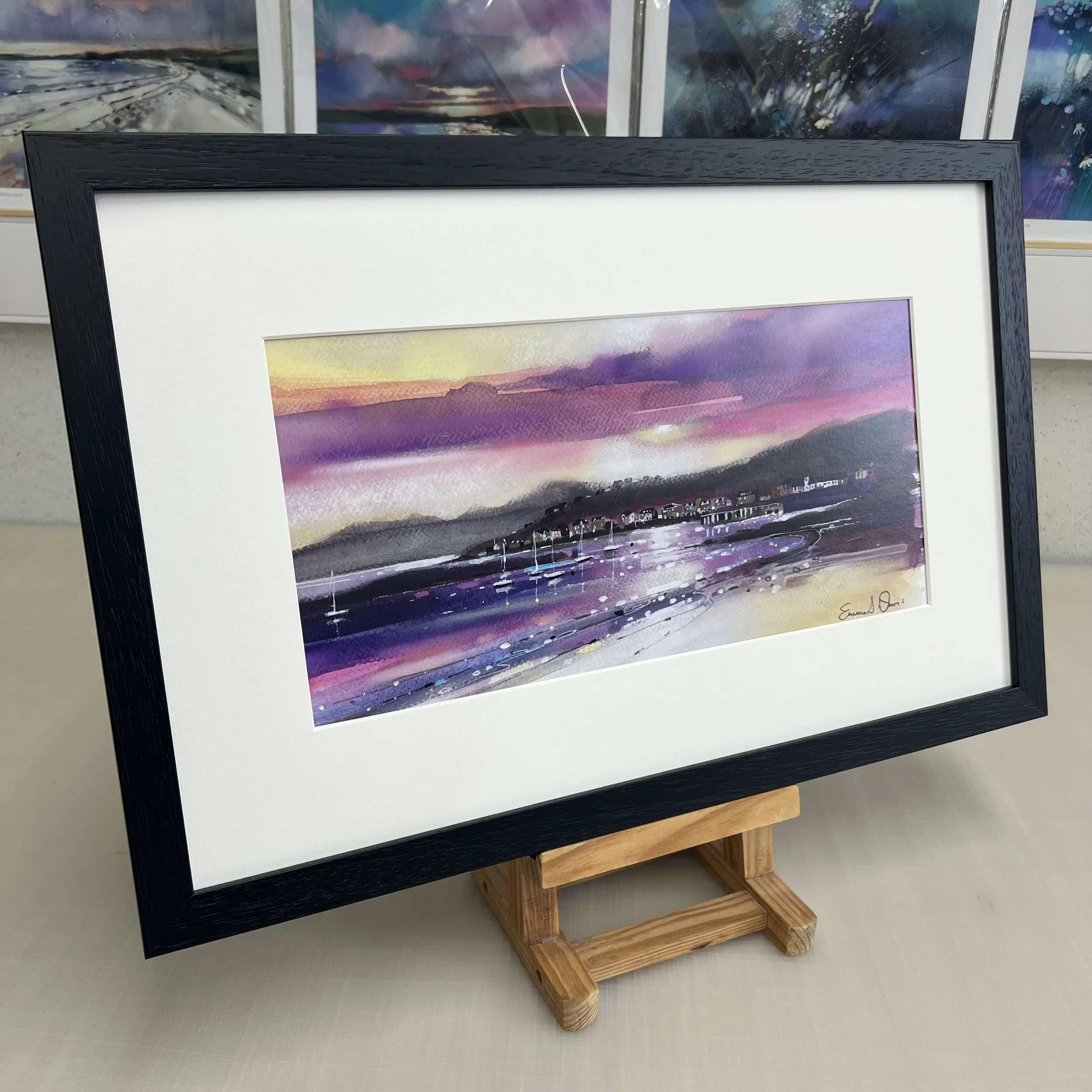 The view from Millport beach looking towards West Bay and Arran beyond on the Isle of Cumbrae, Scotland in Emma S Davis Artist's open edition art print in black frame.