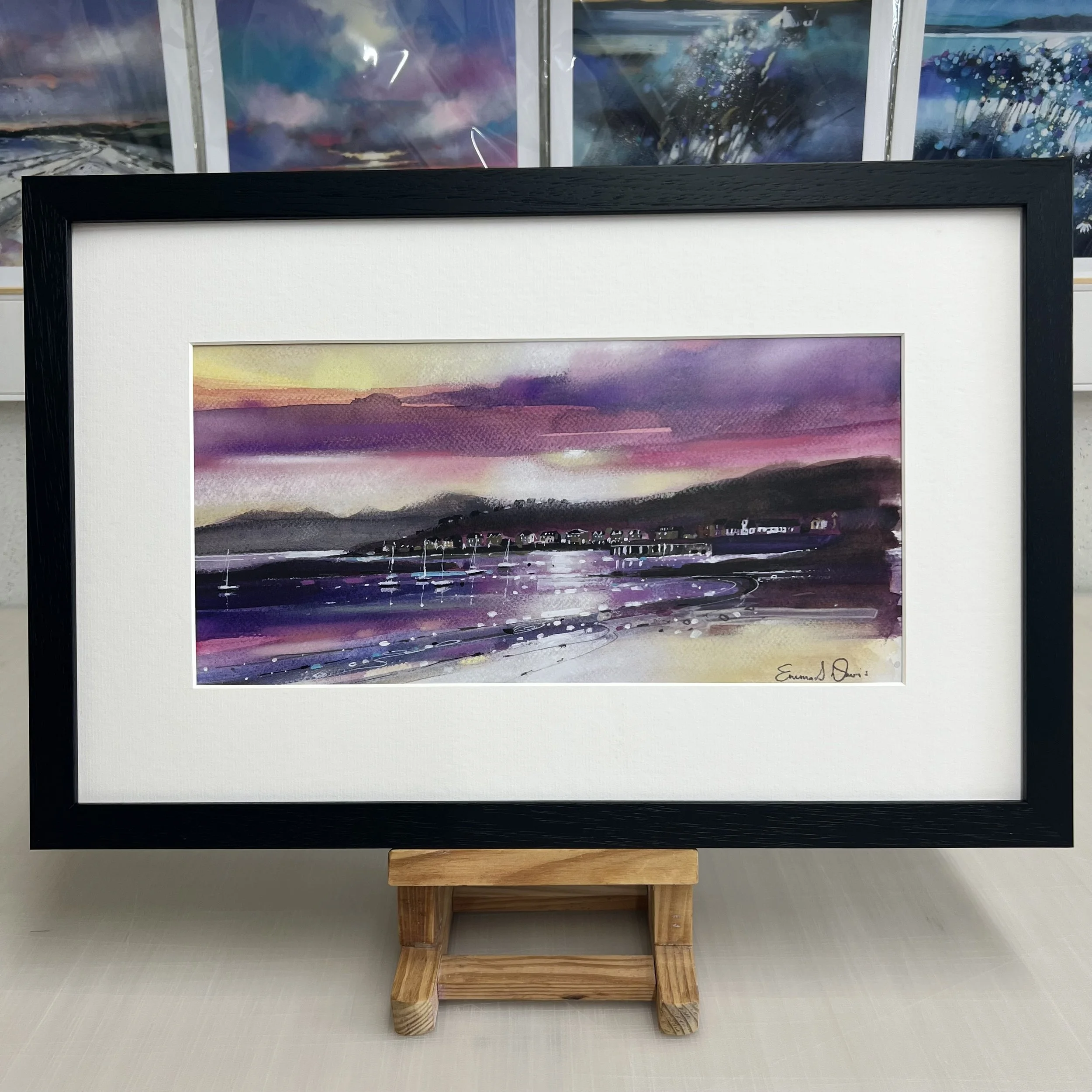 The view from Millport beach looking towards West Bay and Arran beyond on the Isle of Cumbrae, Scotland depicted beautifully in Emma S Davis Artist's open edition art print framed in black.