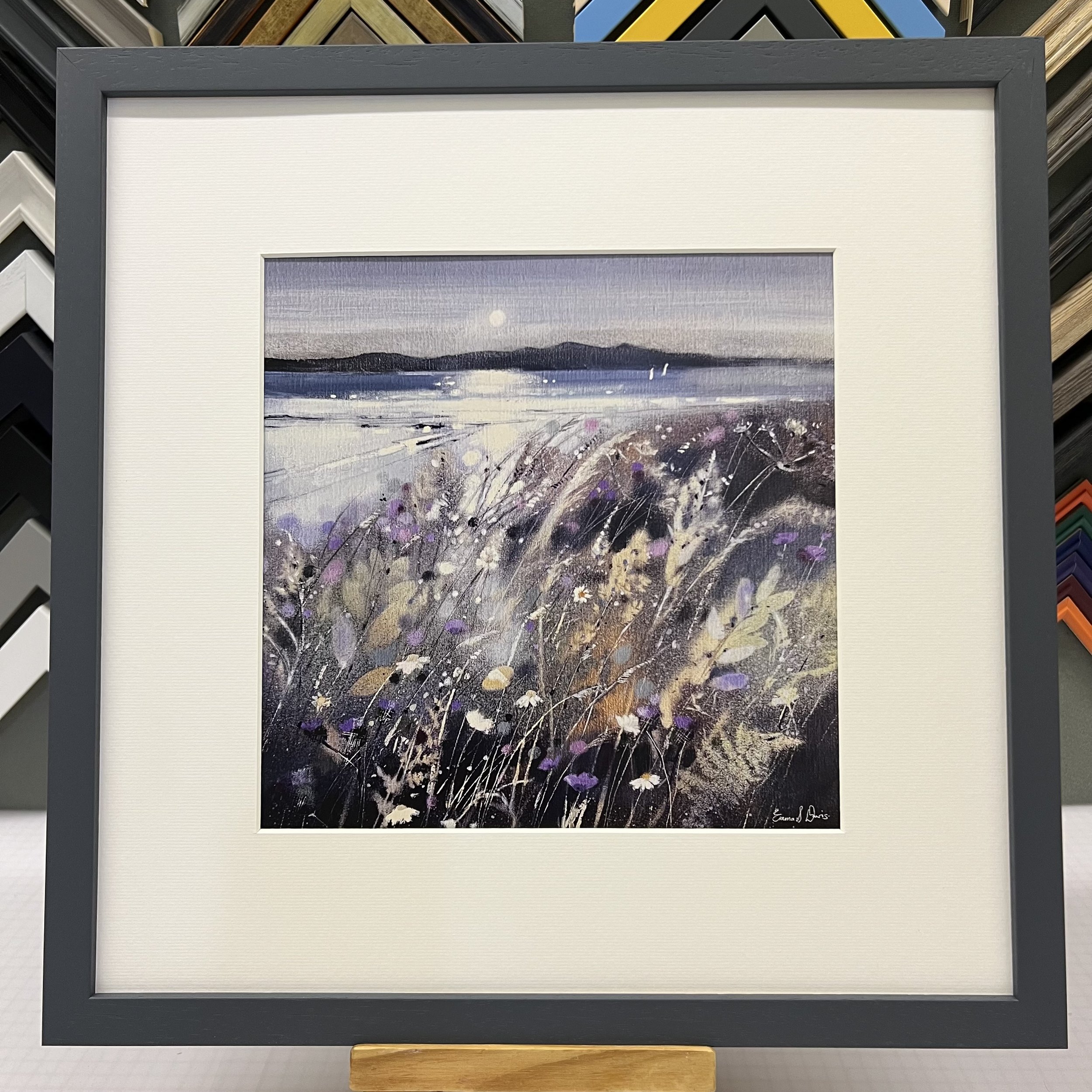 Summer Fields and Arran Open Edition Art Print by Emma S Davis. Presented in a dark grey frame, showcasing Arran on the horizon and wildflowers dancing in the summer breeze.