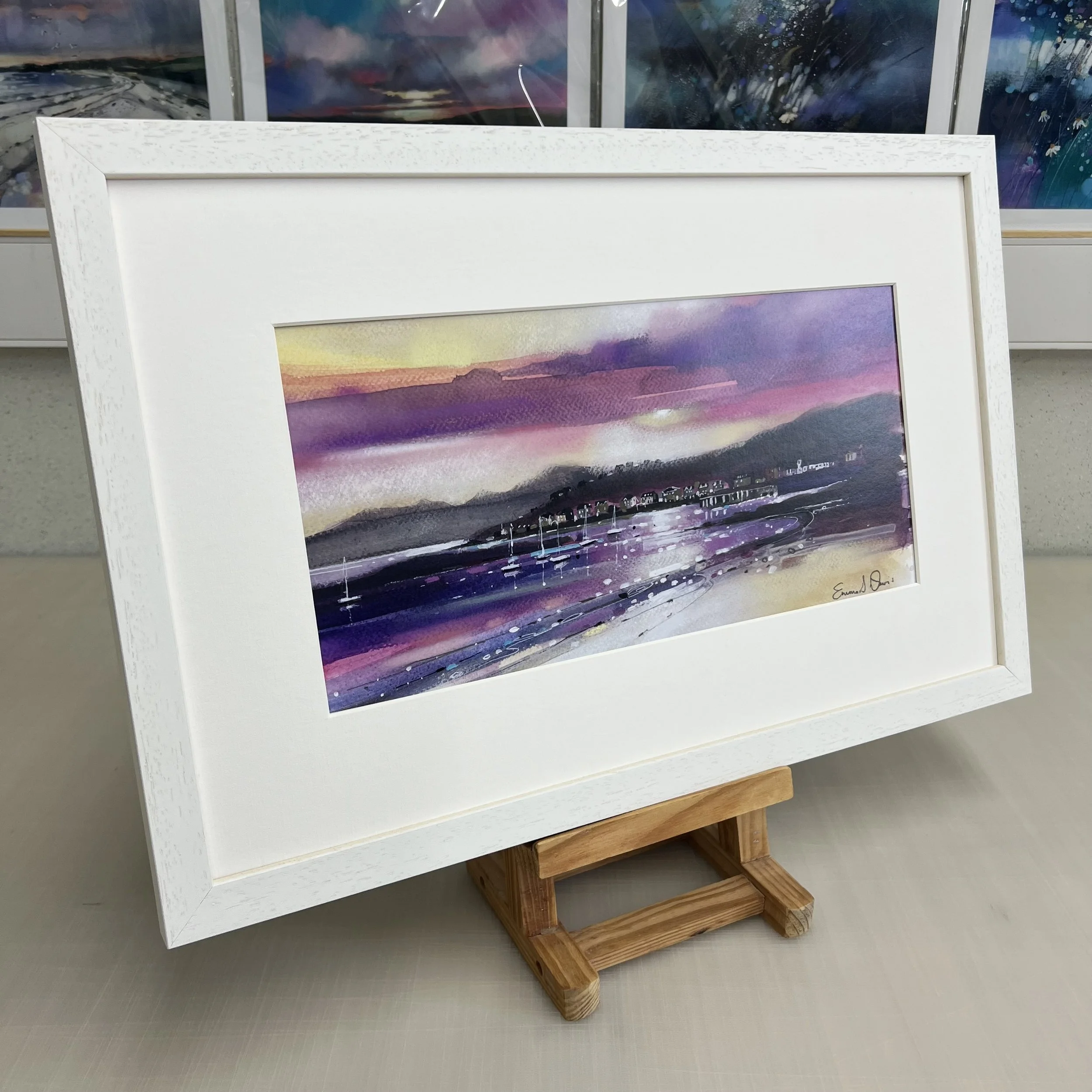 The view from Millport beach looking towards West Bay and Arran beyond on the Isle of Cumbrae, Scotland depicted beautifully in Emma S Davis Artist's open edition art print framed in white.