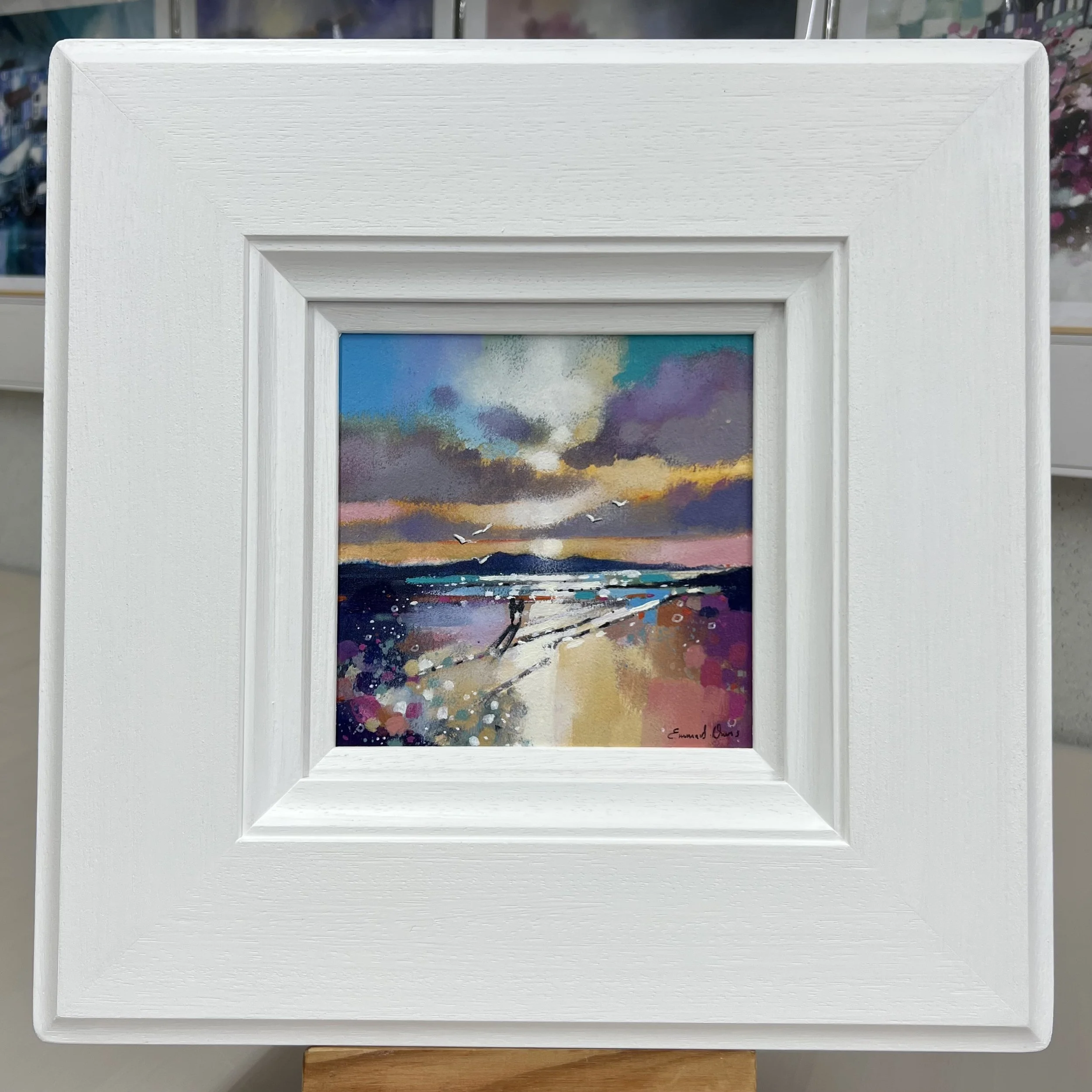 The Isle of Arran's silhouette frames couple walking along Seamill Beach in an original painting by Emma S Davis Artist. Framed in white.