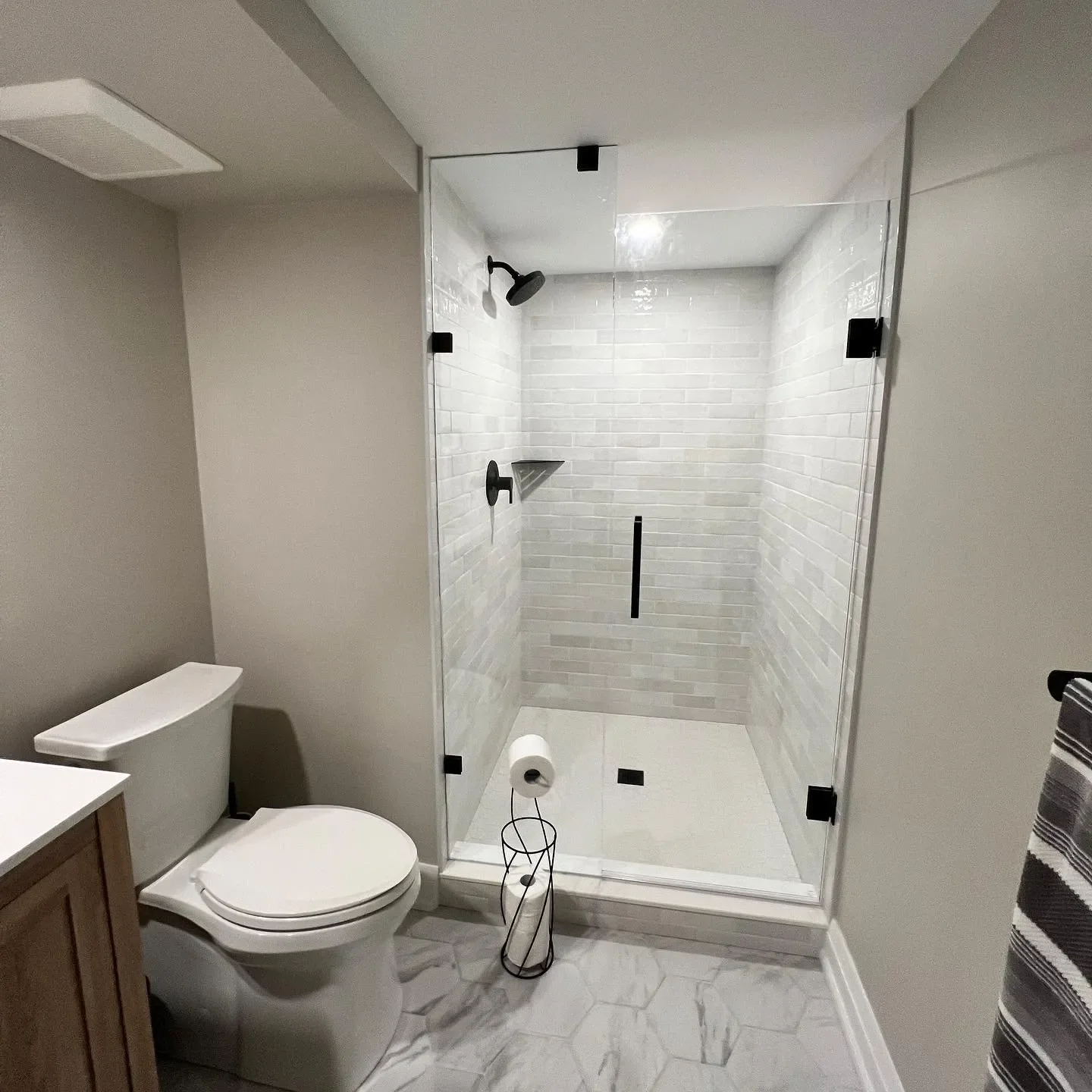 Modern bathroom with a toilet, a glass-enclosed shower with black fixtures, and a striped towel