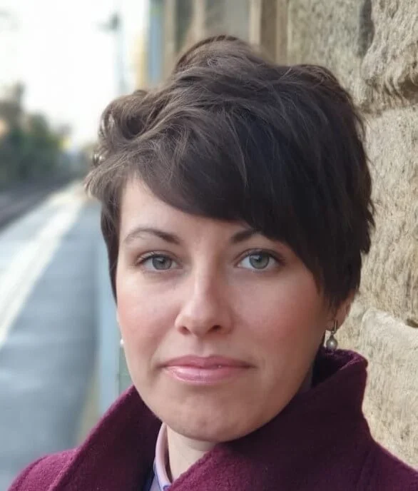 Headshot of Kathryn Welch, with short dark hair and wearing a purple coat
