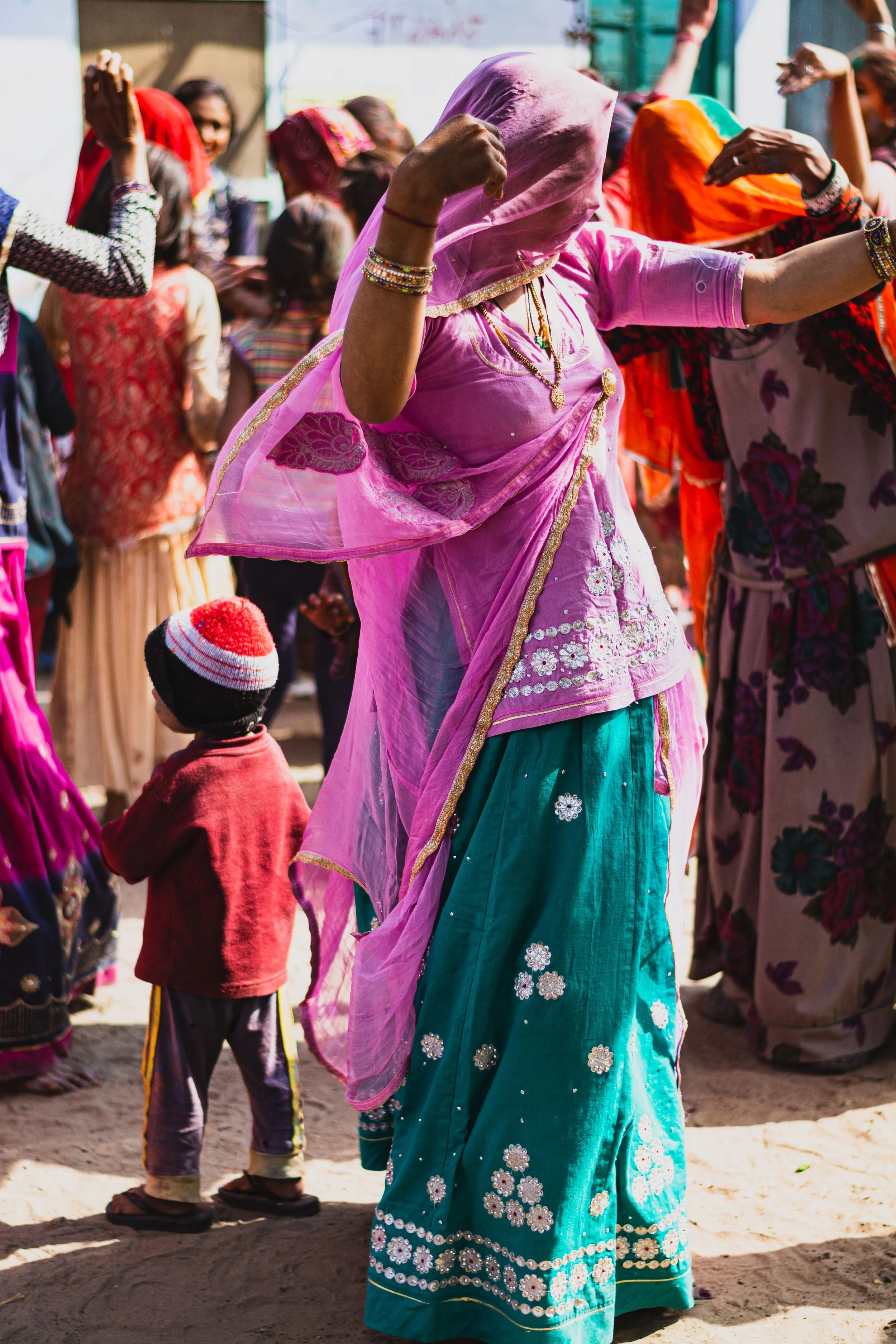 A travel photograph taken in Shyampura in Rajasthan India during Holi celebration showing a woman and children dancing outdoors, with colourful traditional Indian attire.