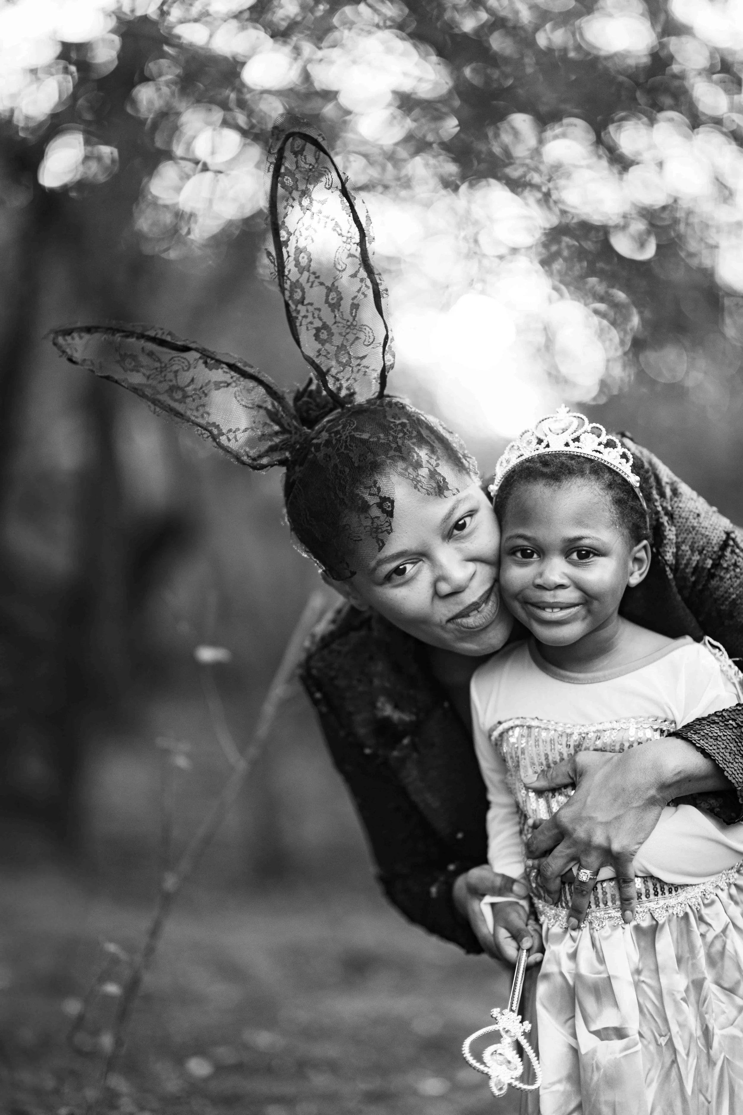 A photoshoot of a mother and daughter in costumes at a birthday party outdoors at the Kruger National Park. The women is wearing lace bunny ears and her daughter a tiara. They are hugging, both smiling for the camera, in a black-and-white photograph.