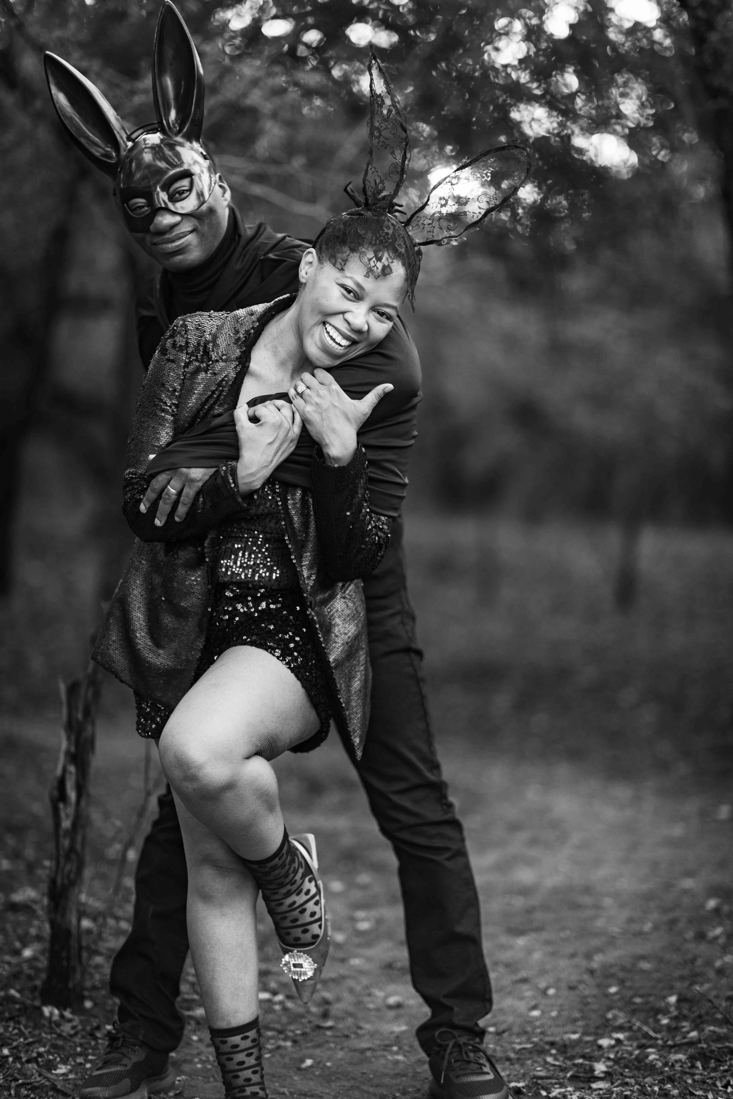 A photoshoot of a couple in costumes at a birthday party, making playful a pose, holding each other and smiling outdoors at the Kruger National Park. The women is wearing rabbit ears and the man a mask.