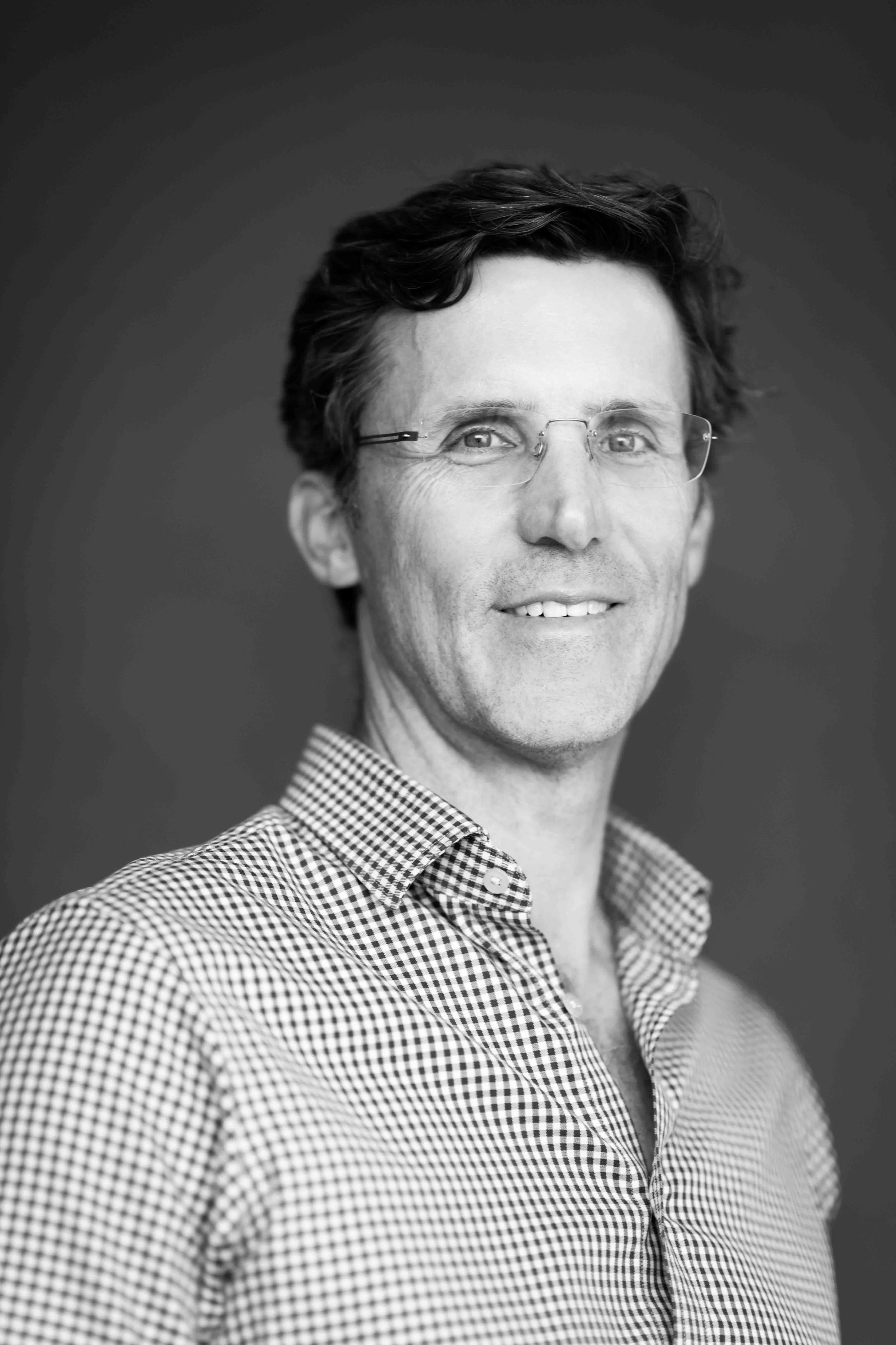 A corporate professional headshot taken in Cape Town in black and white of a man wearing glasses and a checkered button-up shirt, smiling at the camera.