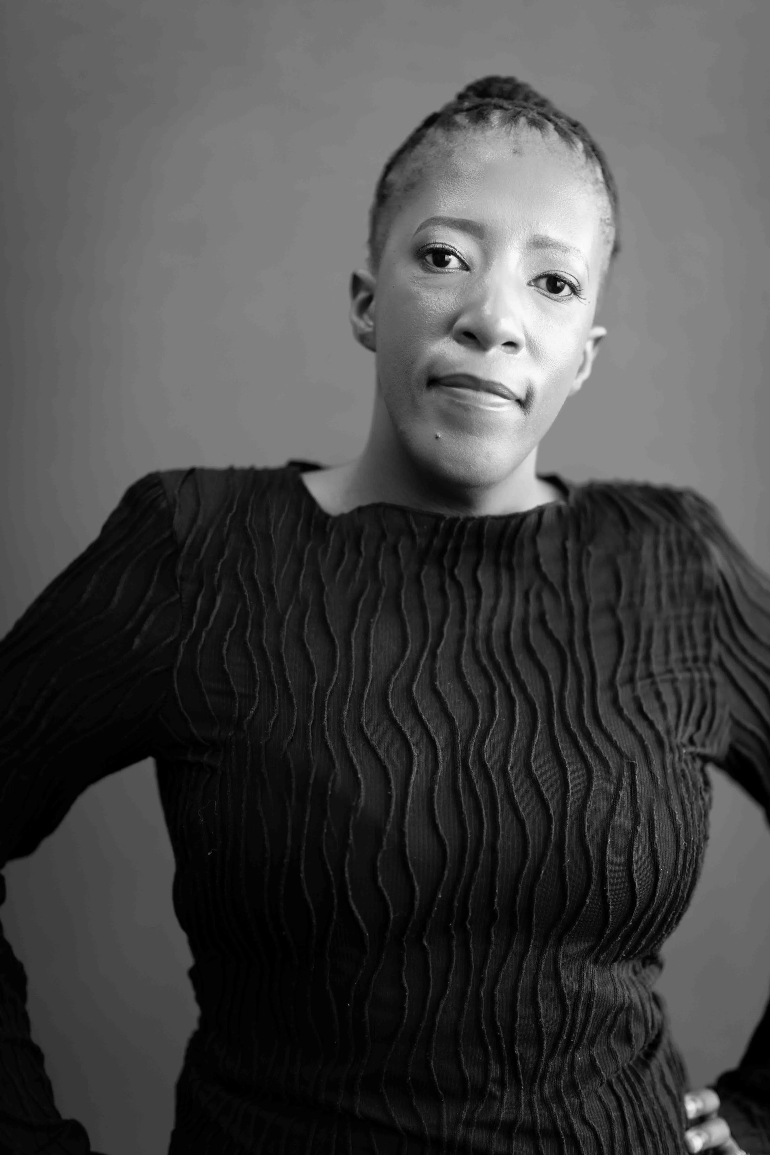 A corporate professional headshot taken in Johannesburg in black and white of a woman with short, styled hair, wearing a textured long-sleeve top, looking confidently at the camera with her hand on her hip.