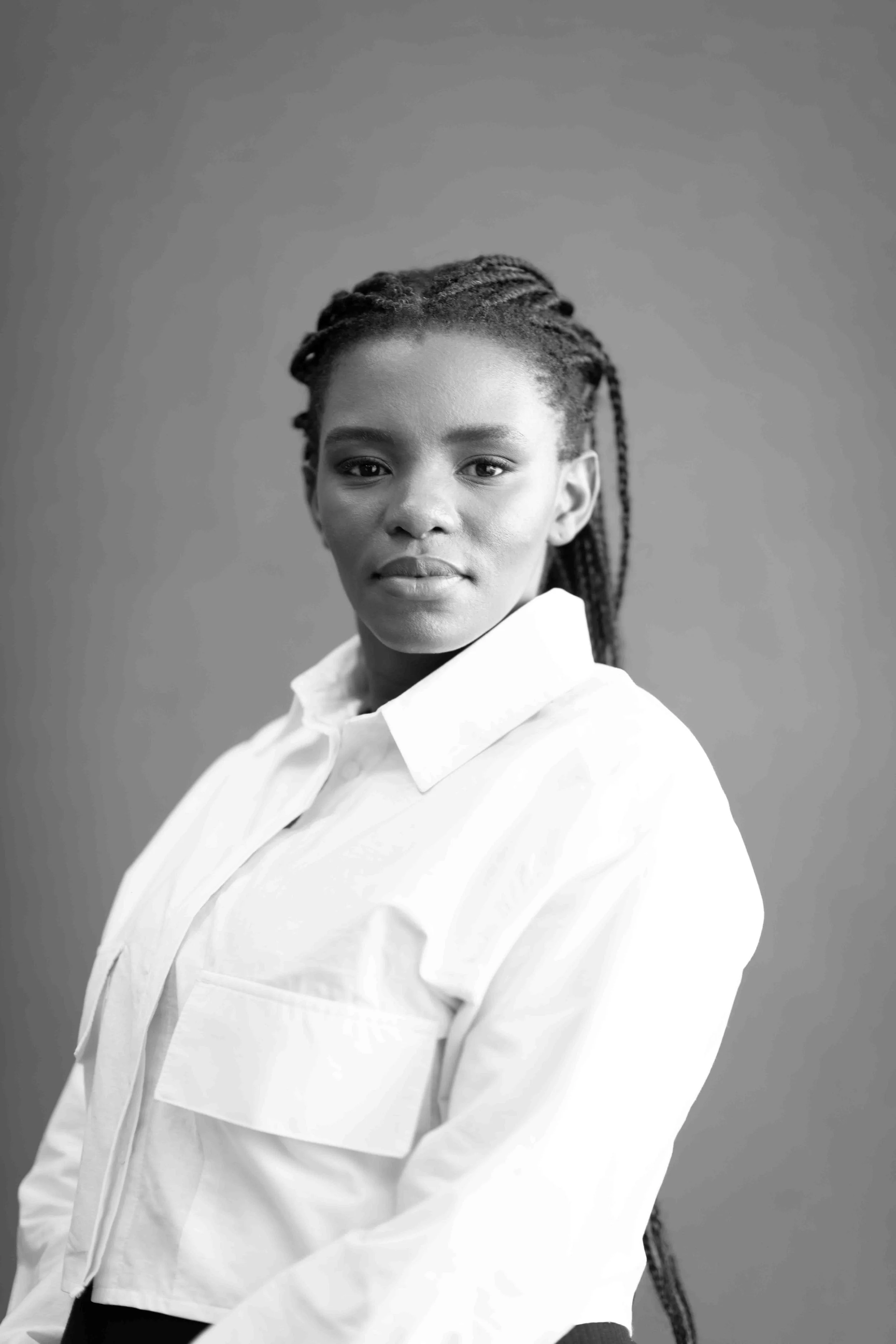 A corporate professional headshot taken in Johannesburg in black and white of a woman with braided hair, wearing a white shirt against a plain backdrop.