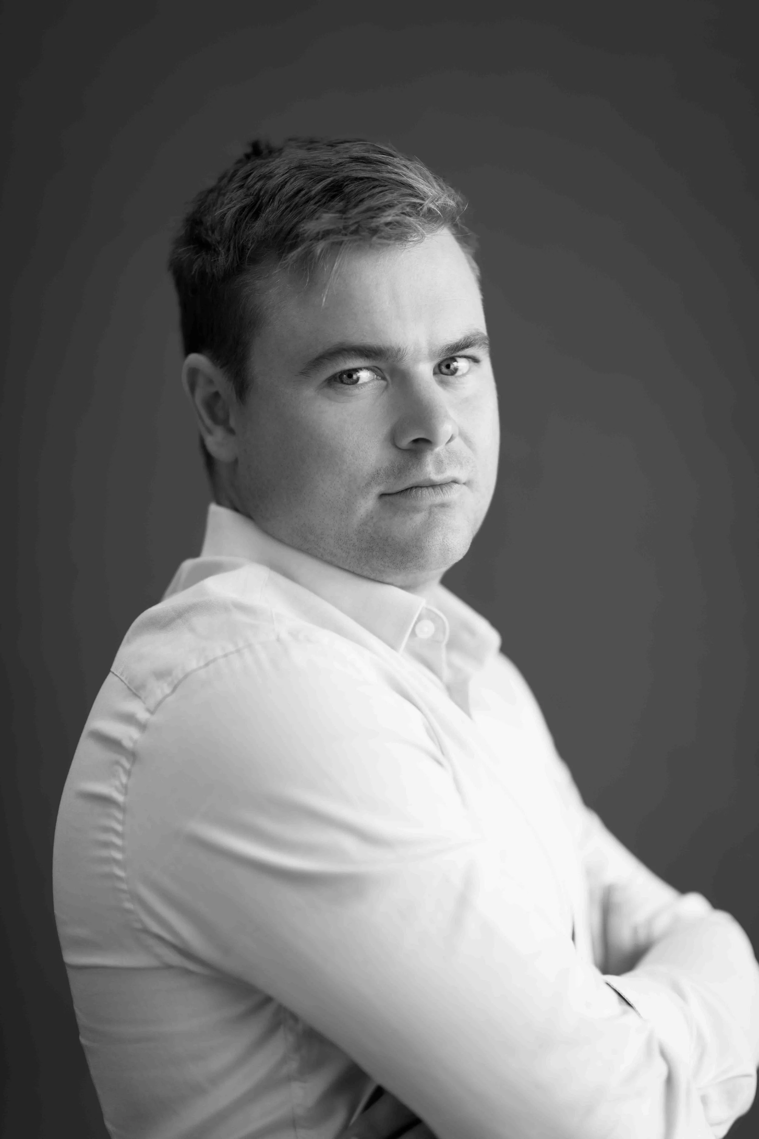 A corporate professional headshot taken in Johannesburg in black and white of a man with short hair, wearing a white shirt, looking at the camera with a serious expression.