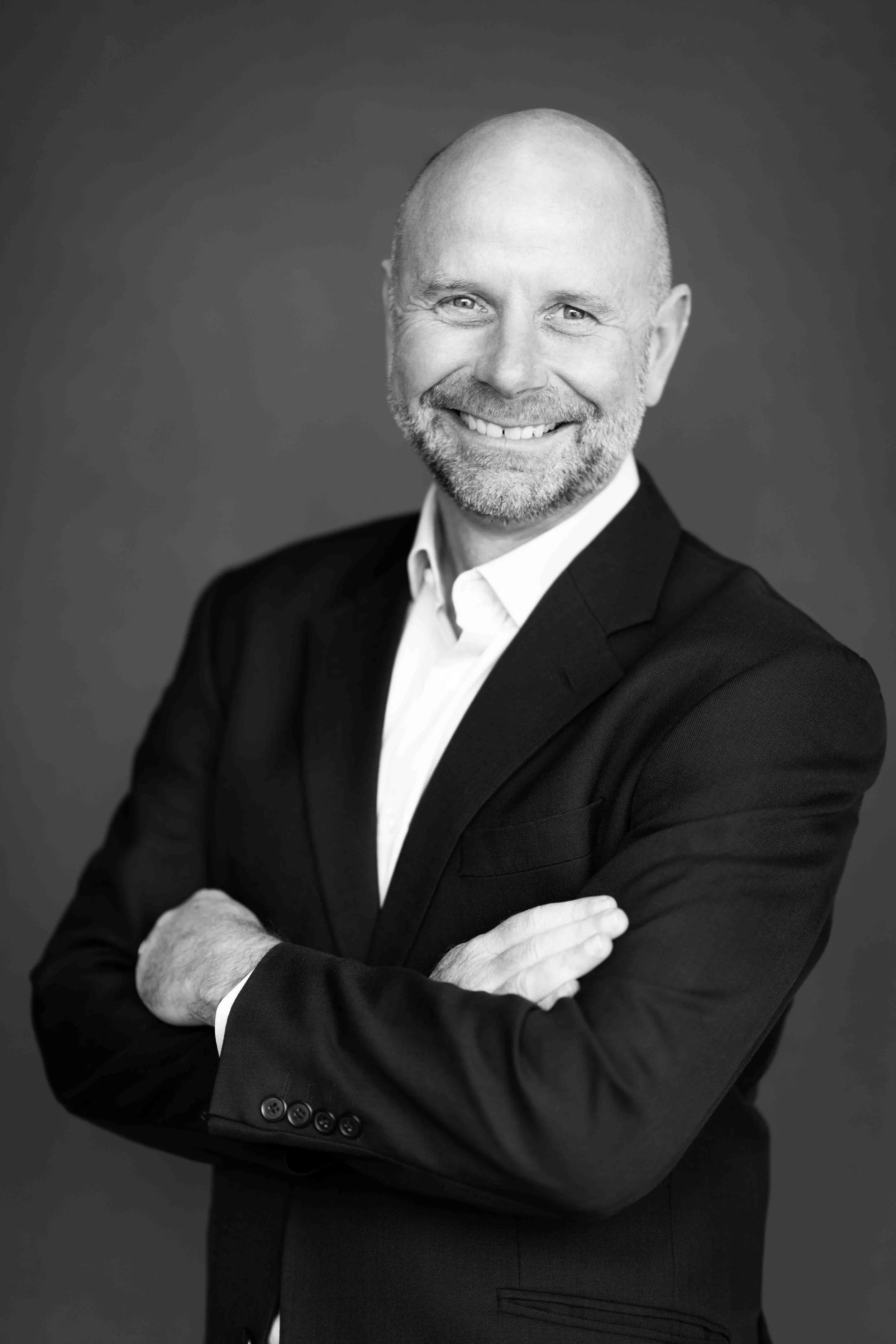 A corporate professional headshot taken in Cape Town in black and white of a smiling man with a beard, dressed in a suit with arms crossed.