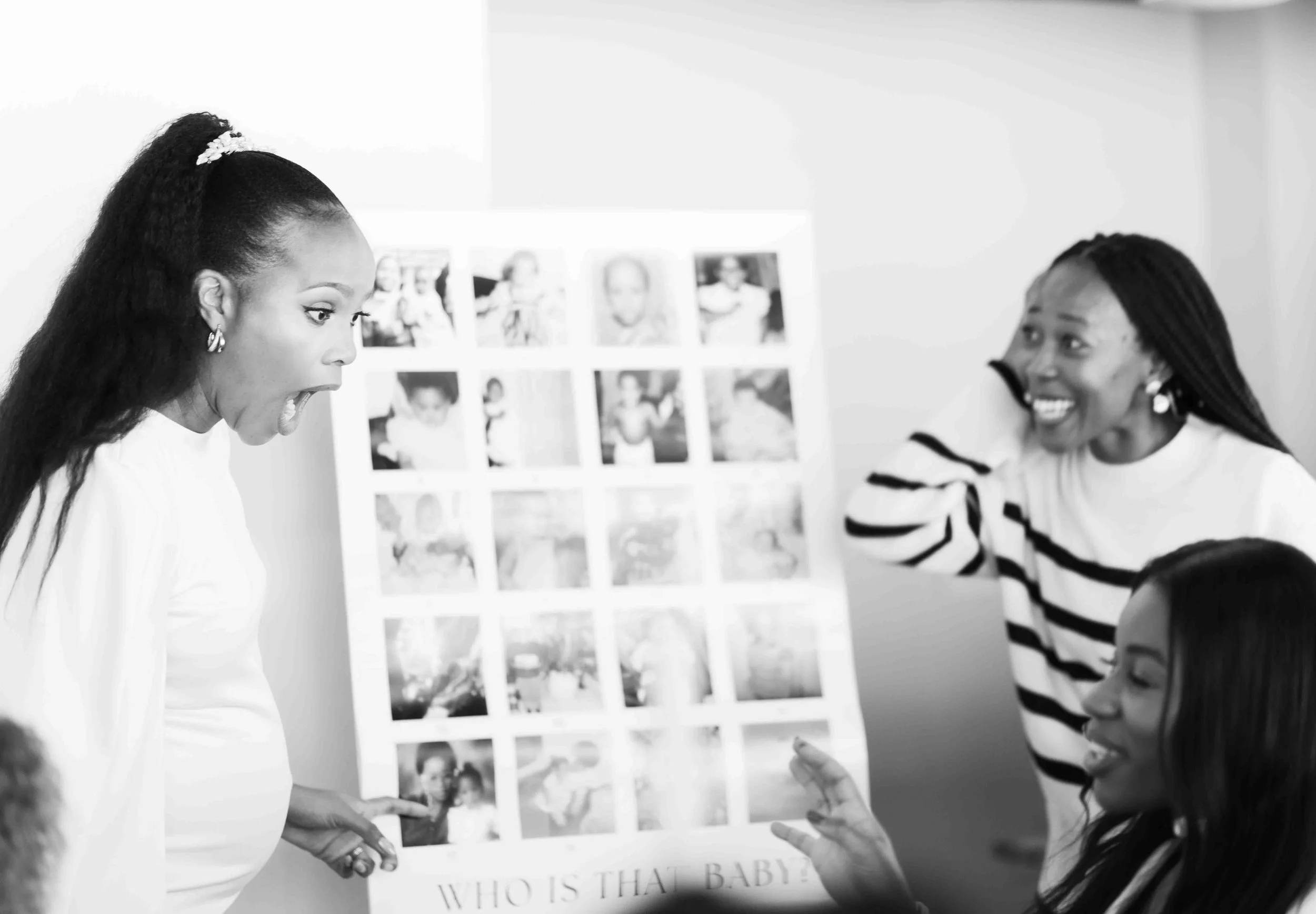 A black and white photograph taken during a baby shower event showing two woman playing a baby shower game where you have to guess who the child is by looking at their childhood photos.
