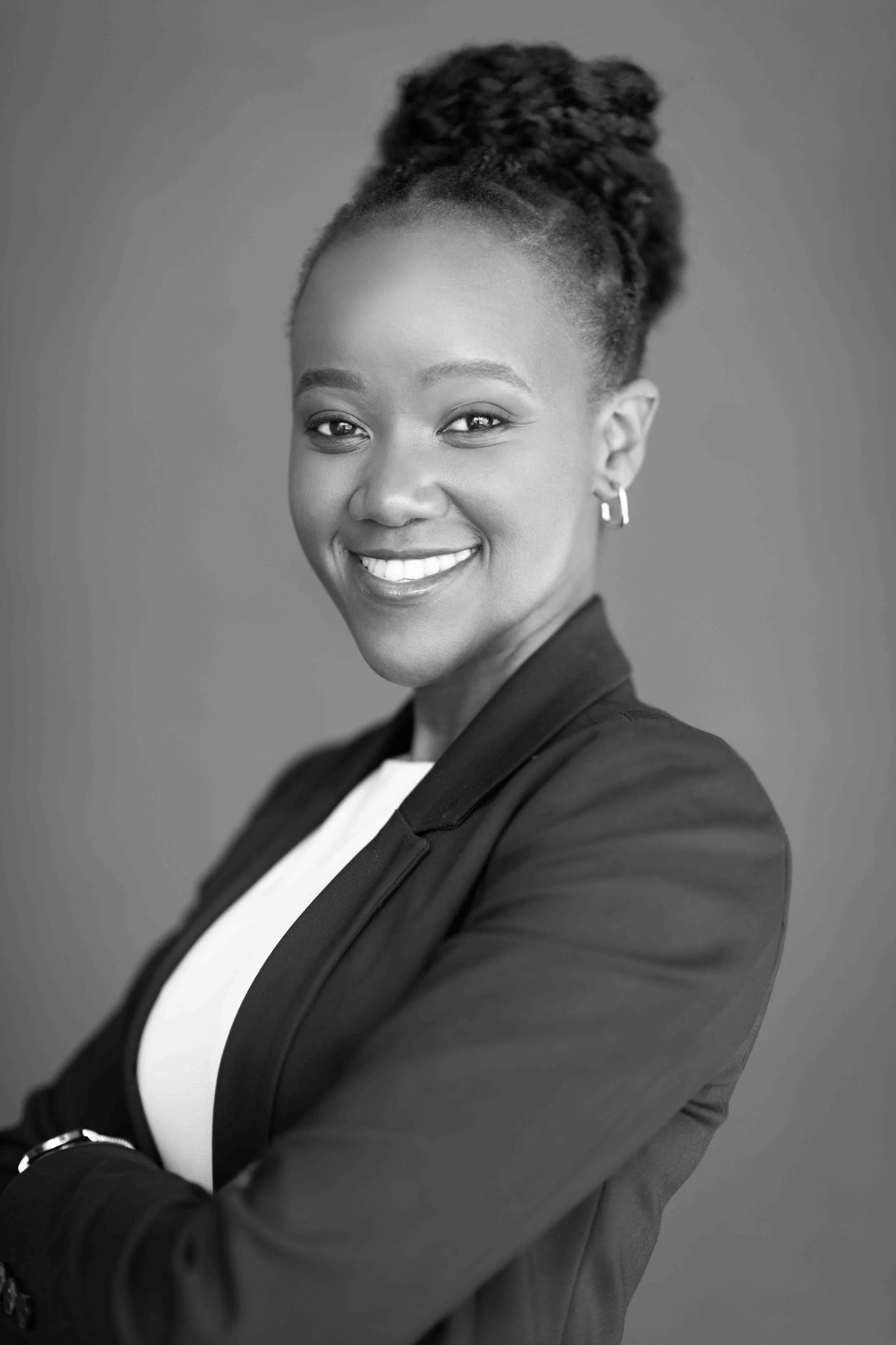 A corporate professional headshot taken in Cape Town in black and white of a woman smiling, with her arms crossed, in business attire, with her hair styled in an updo.