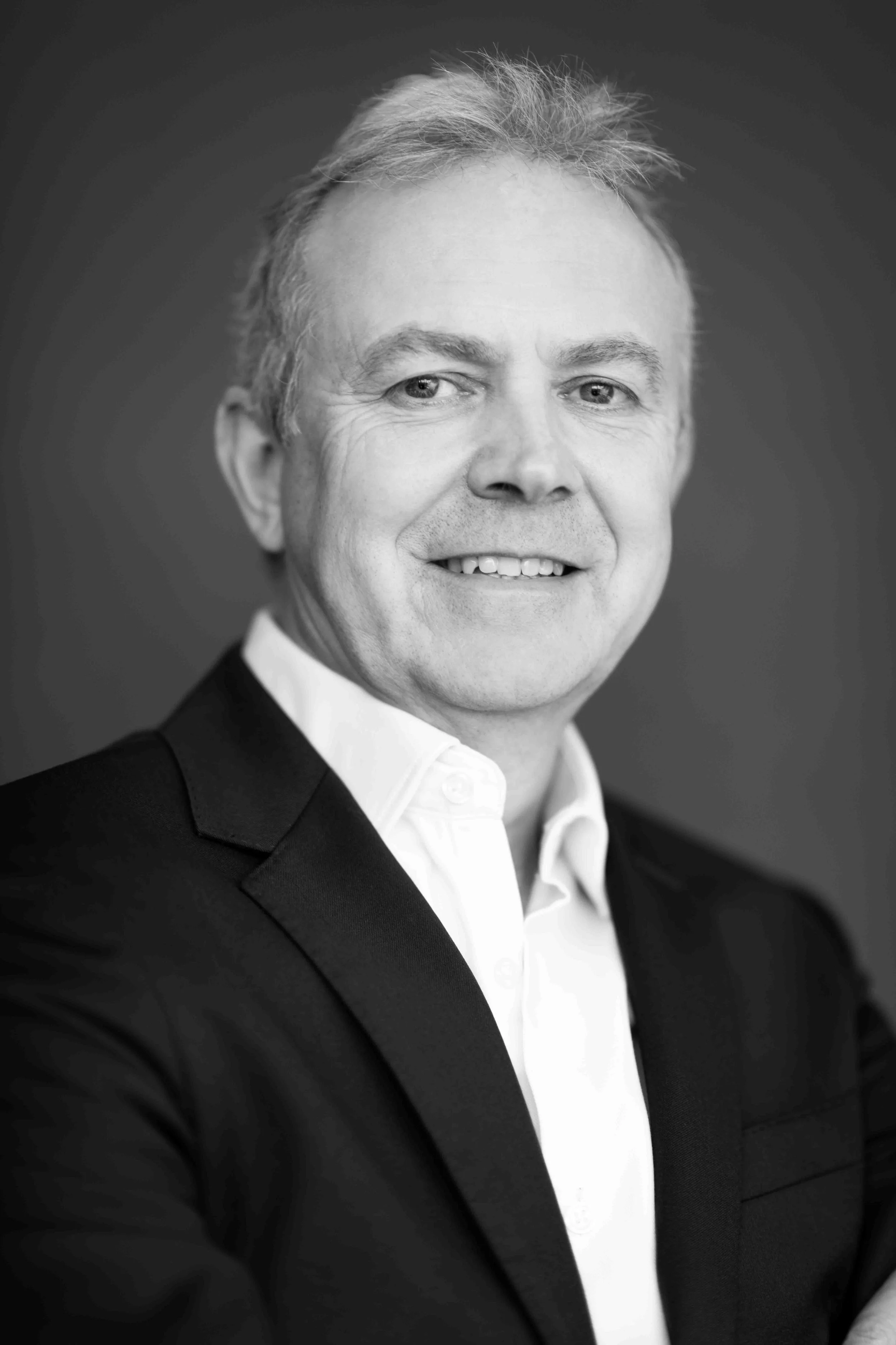 A corporate professional headshot taken in Cape Town in black and white of a smiling man wearing a suit and white shirt, with short hair and light skin.