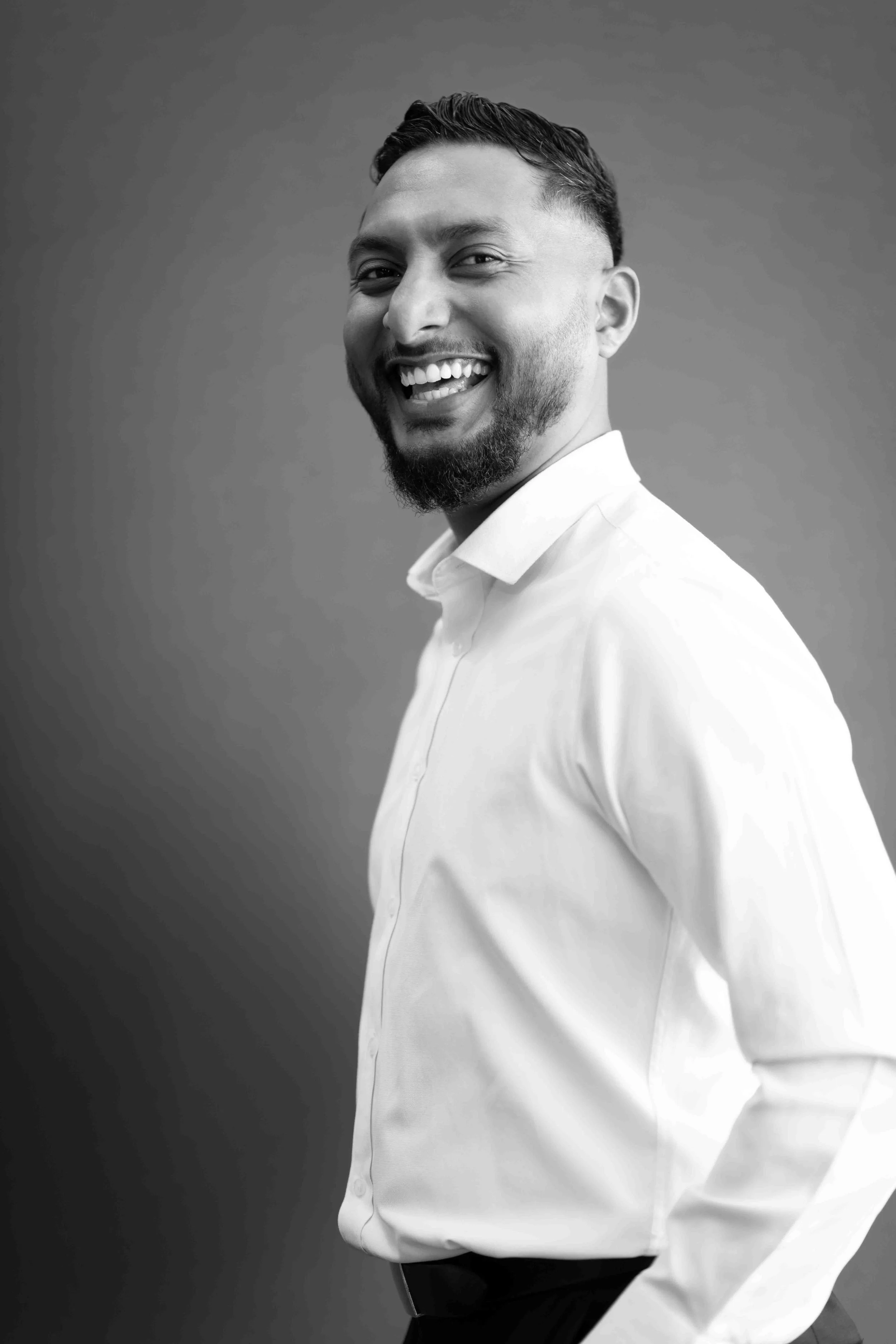 A corporate professional headshot taken in Johannesburg in black and white of a smiling man wearing a white shirt, looking at the camera.