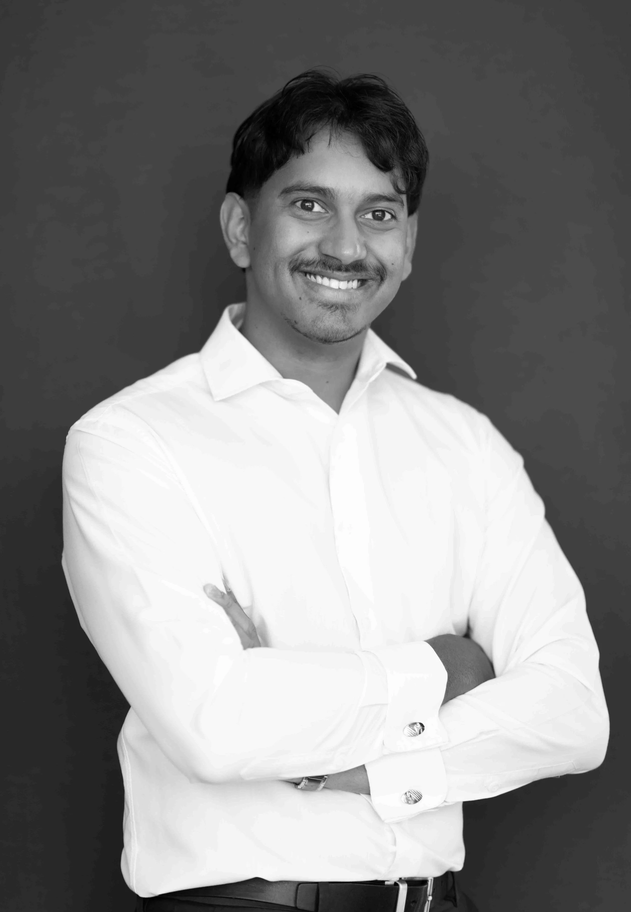 A corporate professional headshot taken in Cape Town in black and white of a man smiling with arms crossed, wearing a white dress shirt against a dark background.