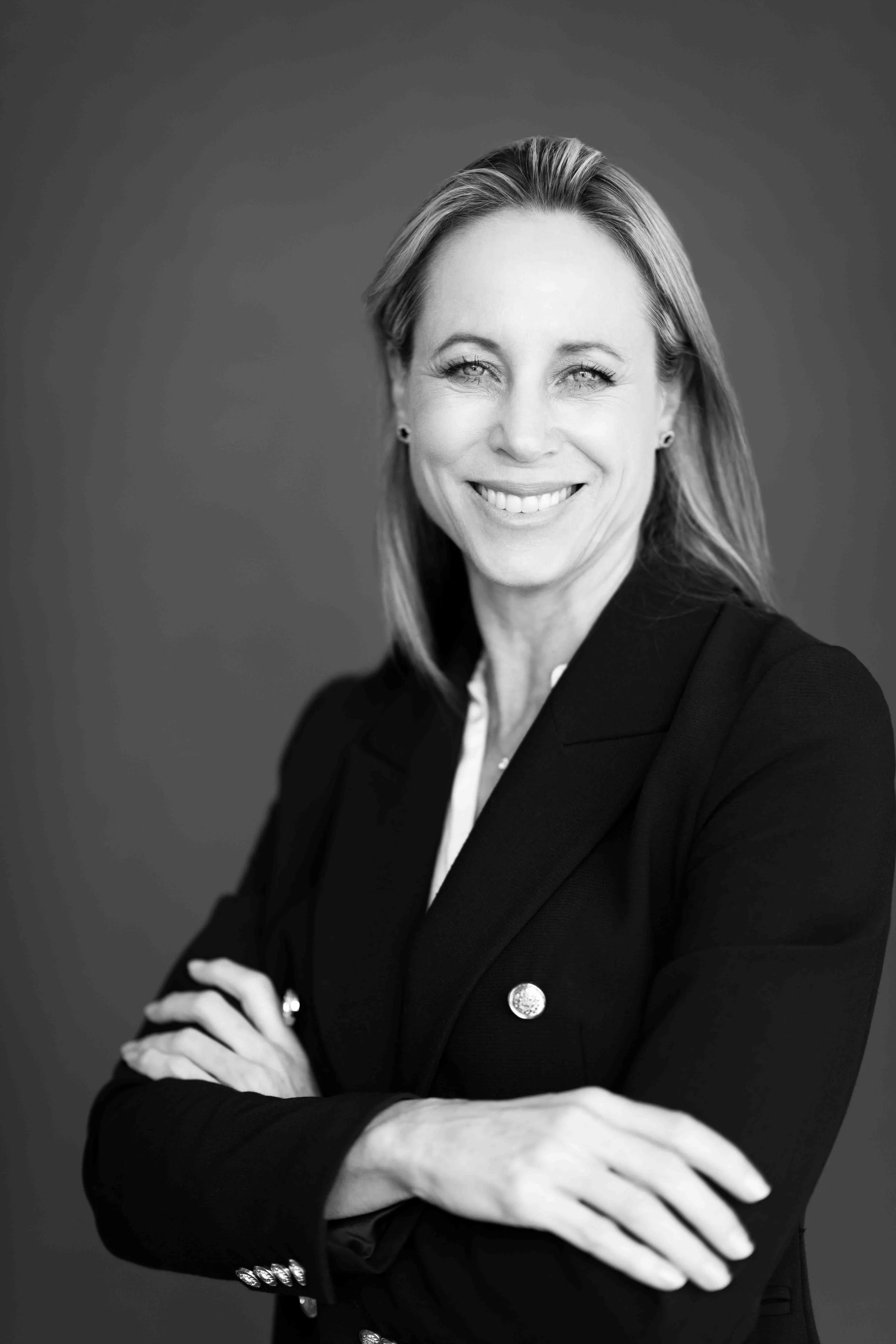 A corporate professional headshot taken in Cape Town in black and white of a woman smiling with arms crossed, wearing a blazer.