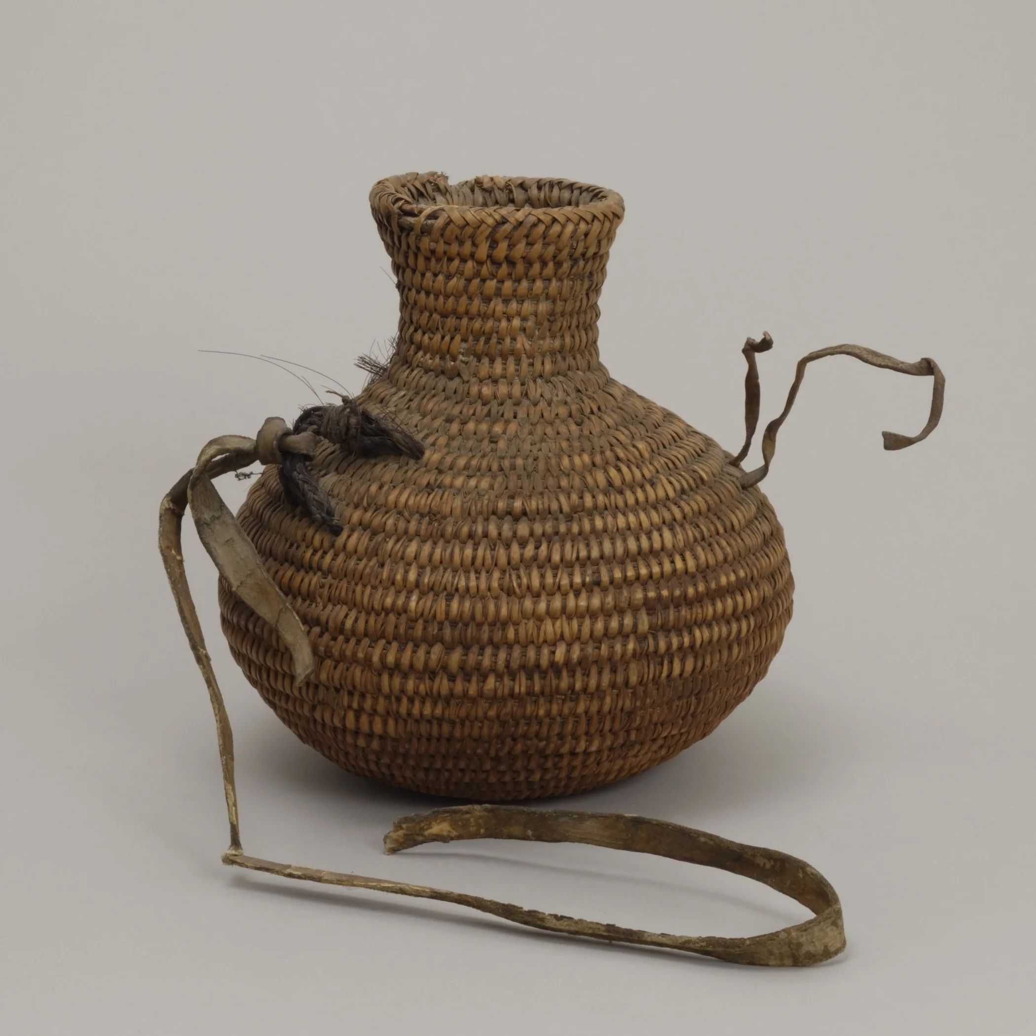 Jicarilla Apache, coil-basket water bottle, collected 1887–1906. Plant fiber, horse hair, and leather, 8 11/16 × 8 1/16 in. Hood Museum of Art, Dartmouth College: Gift of Mrs. Ida Farr Miller; 44.18.8779.