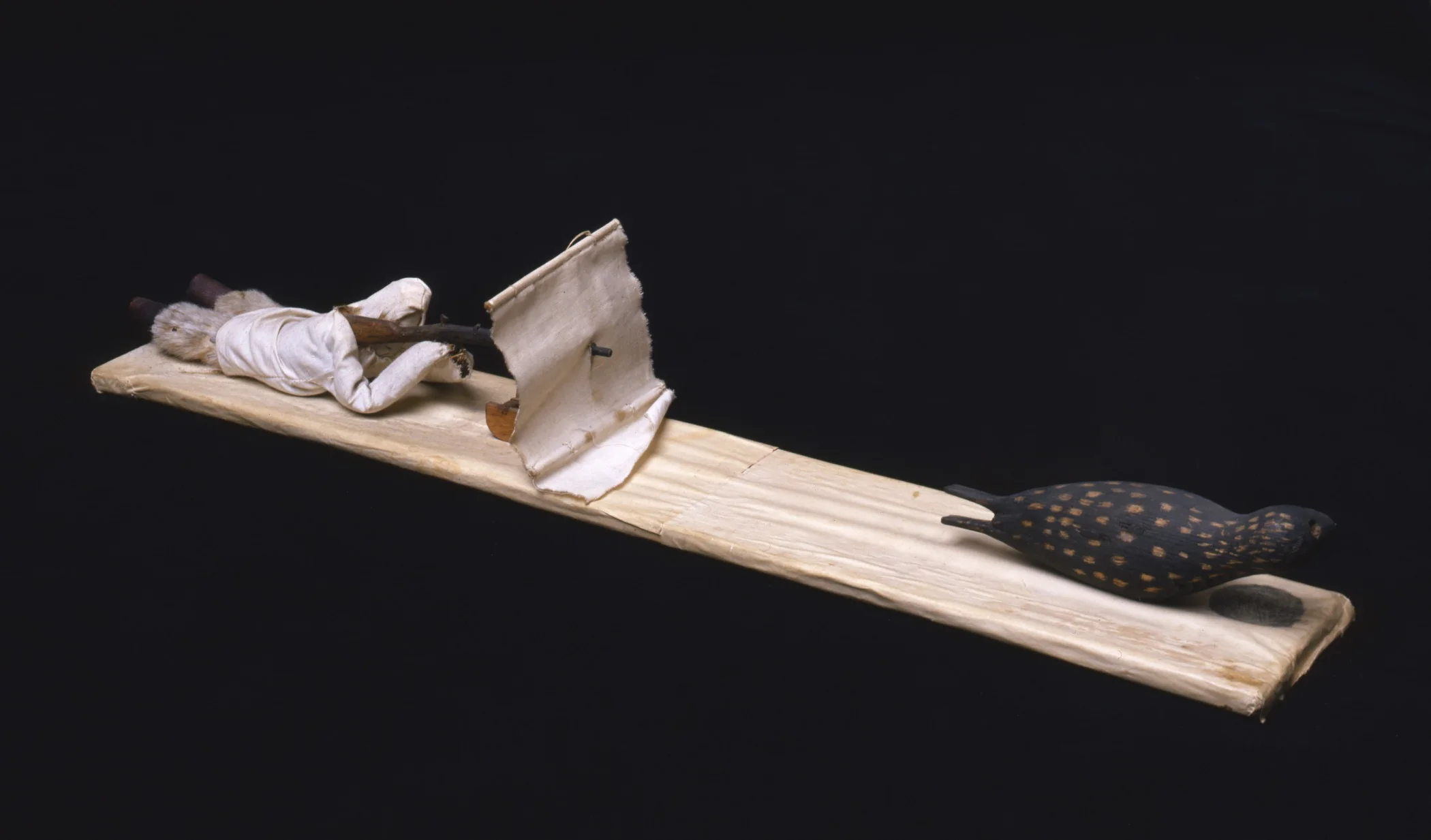 Kalaallit (West Greenlandic Inuit), souvenir model of a man seal hunting in the spring using a blind and a gun stand, early 1930s. Wood, paper, cloth, seal fur, sealskin, commercial thread, and glue, 2 9/16 × 3 3/4 × 22 13/16 in. Hood Museum of Art, Dartmouth College: Gift of George Murphy, Class of 1941; 39.70.7906.