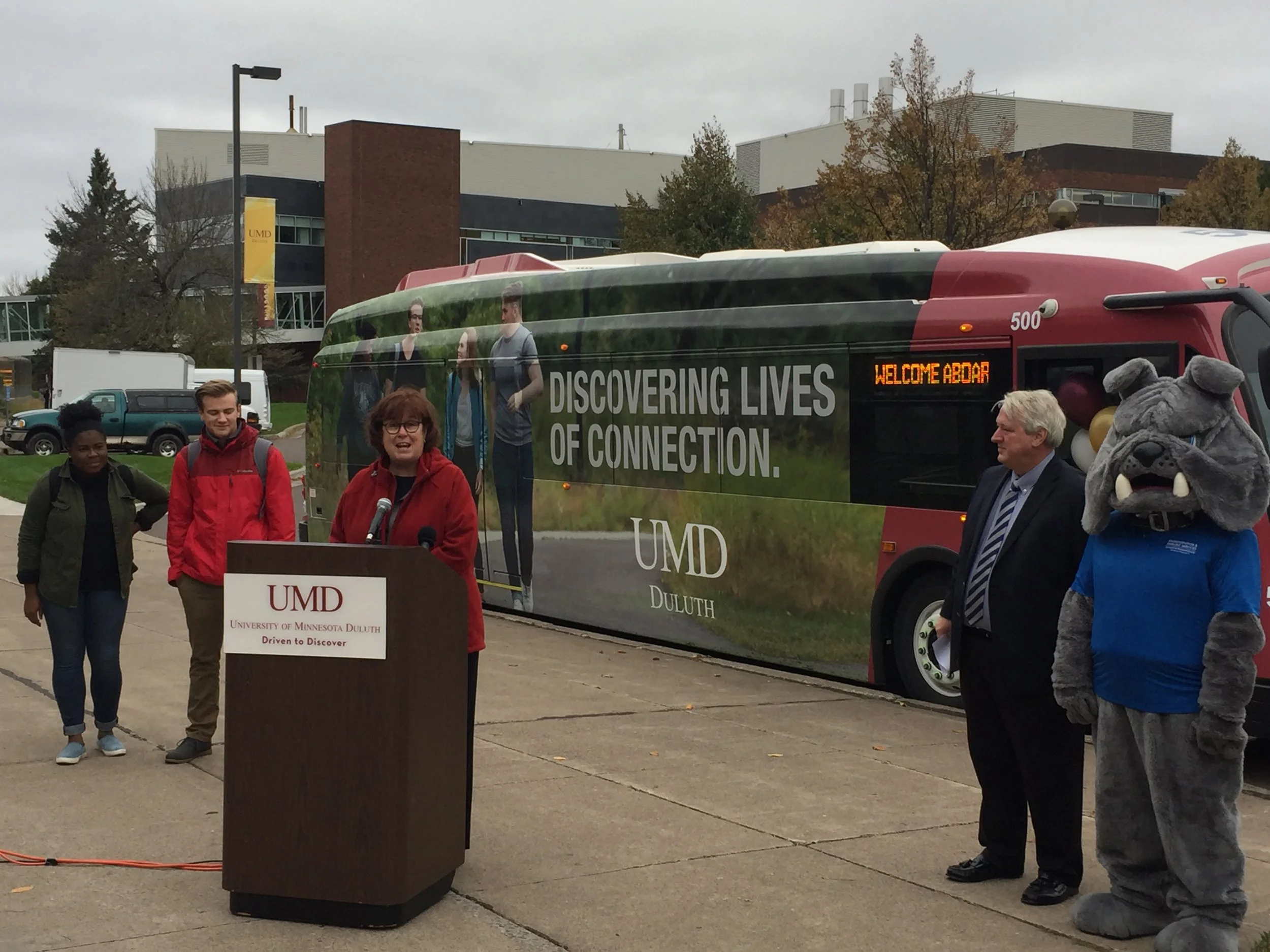Lisa Erwin, the Vice Chancellor for Student Life and Dean of Students, leads the unveiling of the new electric bus. Pictured with Champ, students featured on the bus, and DTA General Manager Phil Pumphrey. Photo courtesy of Corbin Smyth.