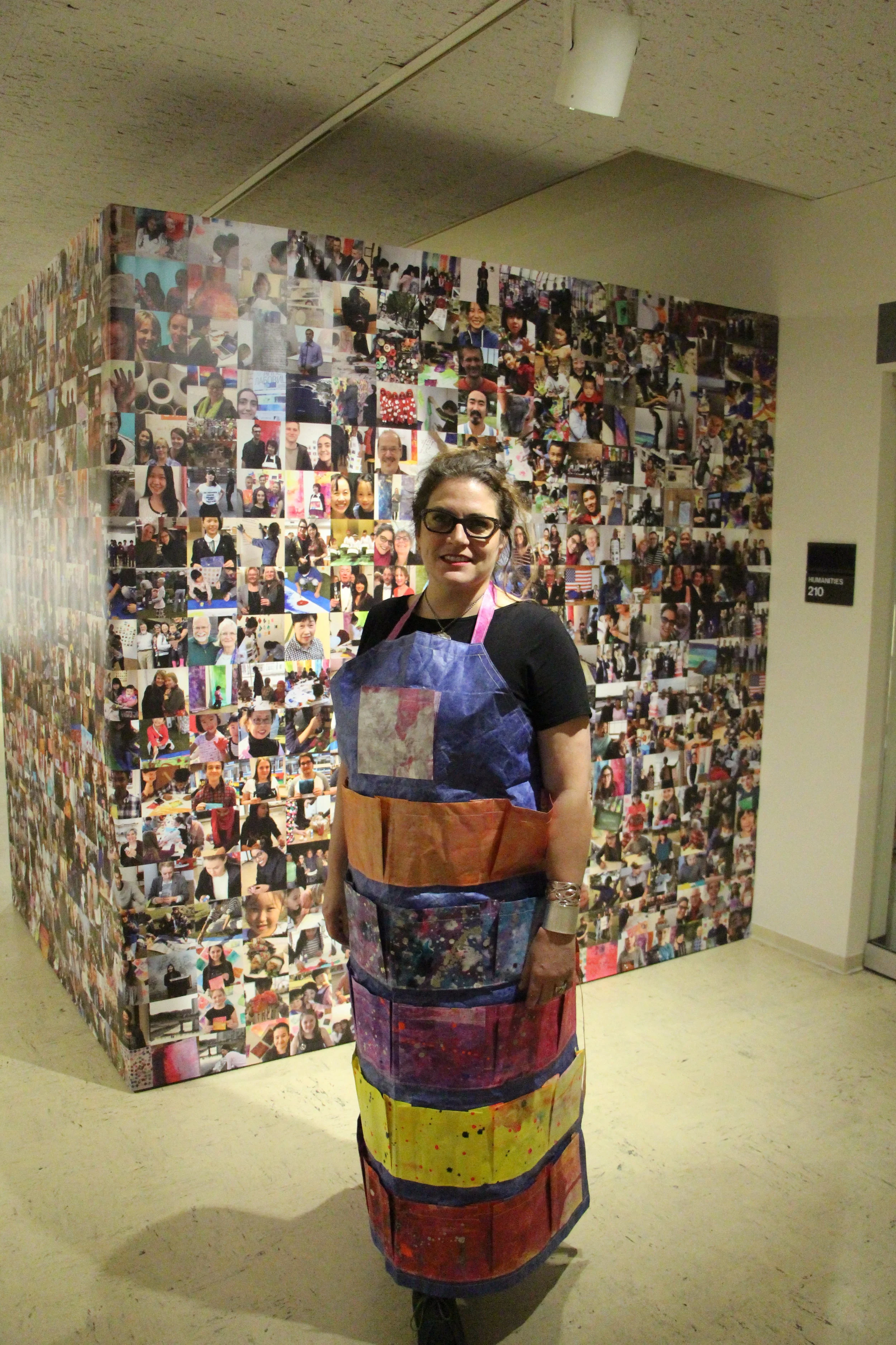 Labovitz wearing a “celestial generosity apron” standing in front of pictures from her art workshops. Photo by Jakob Bermas