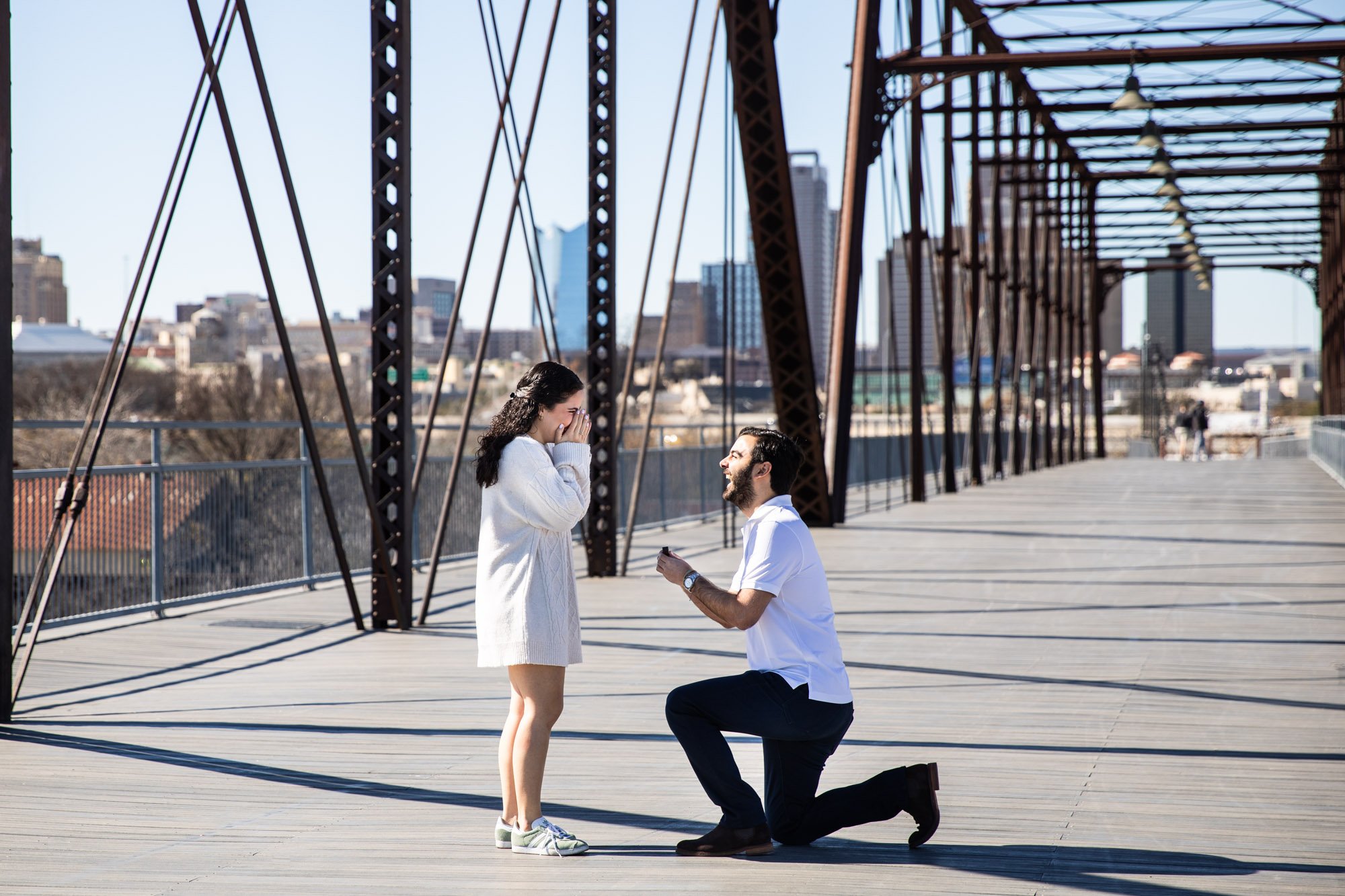 Man on one knee proposing to woman on Hays Street Bridge by San Antonio engagement photographer, Kelly Williams