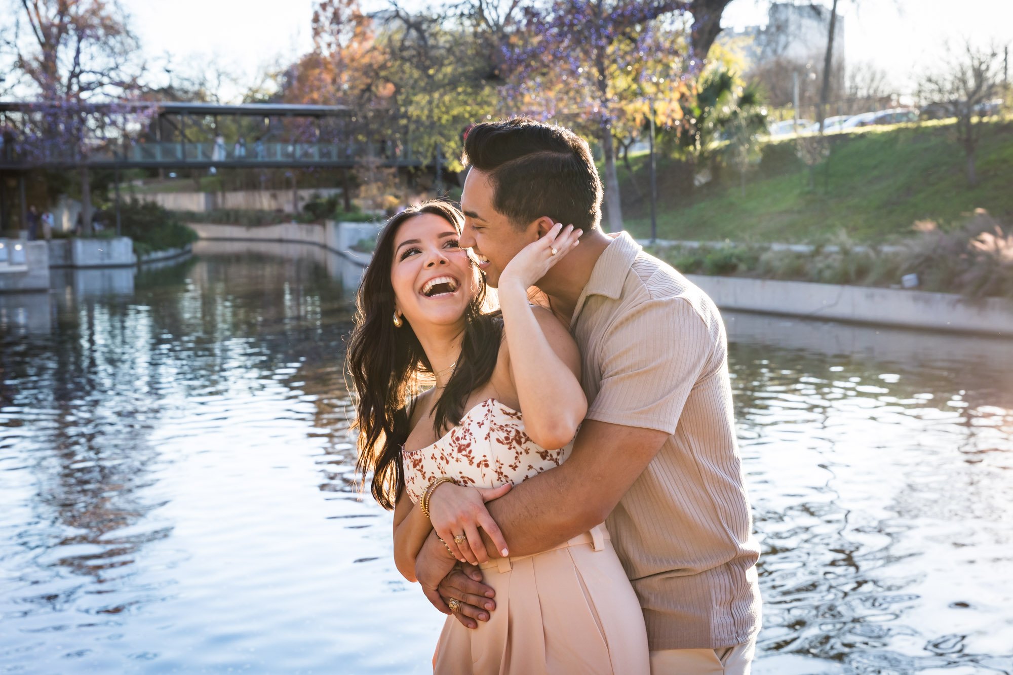 Man kissing woman on the cheek in front of Riverwalk by San Antonio engagement photographer, Kelly Williams