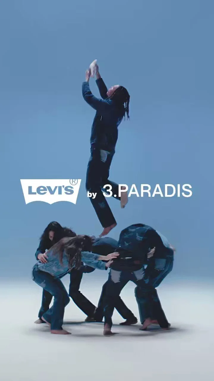 Multiple people forming a human tower with a person standing on top, against a blue background, logo of Levi's and text 'by 3. PARADIS', fashion campaign