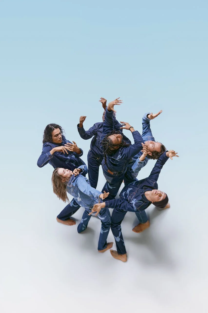 A group of six women dressed in denim clothing are dancing together against a light blue background, with their arms and bodies positioned in expressive dance poses, Levi's Fashion Campaign