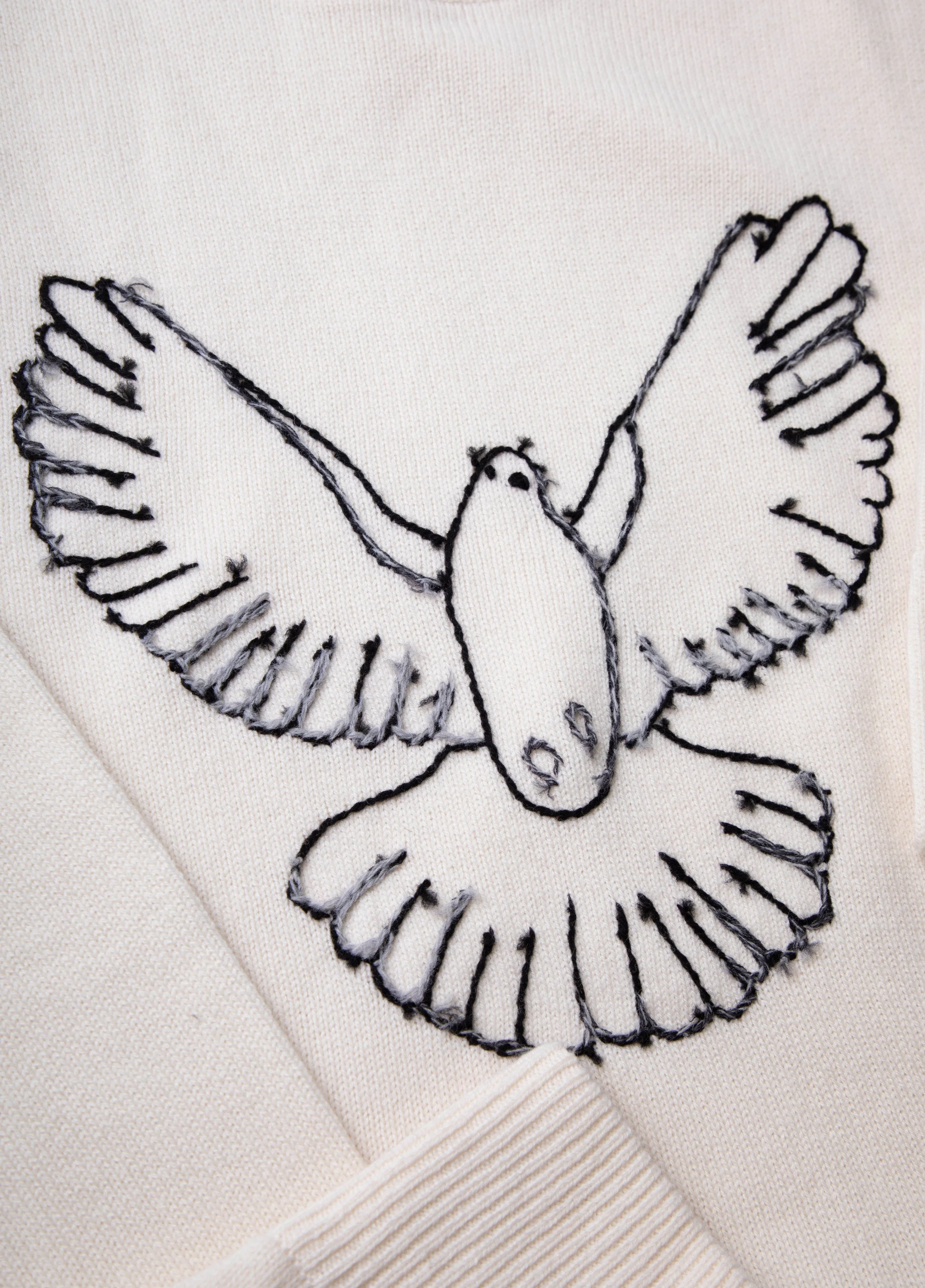 Embroidery of a bird with outstretched wings on a cream-colored fabric.