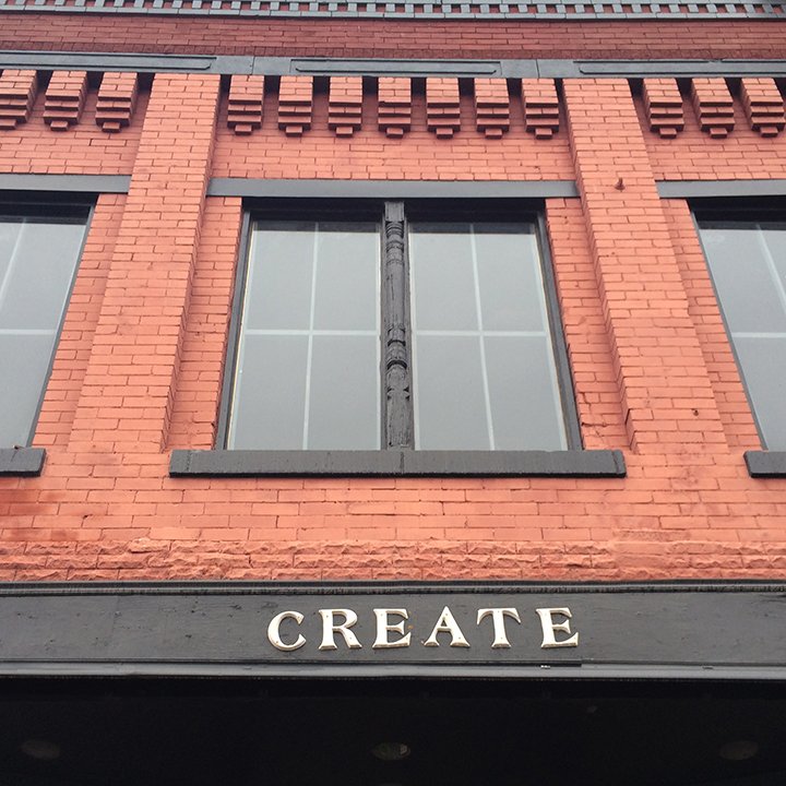 Front view of a red brick building with black window frames and the word "CREATE" in capital letters above a black awning.
