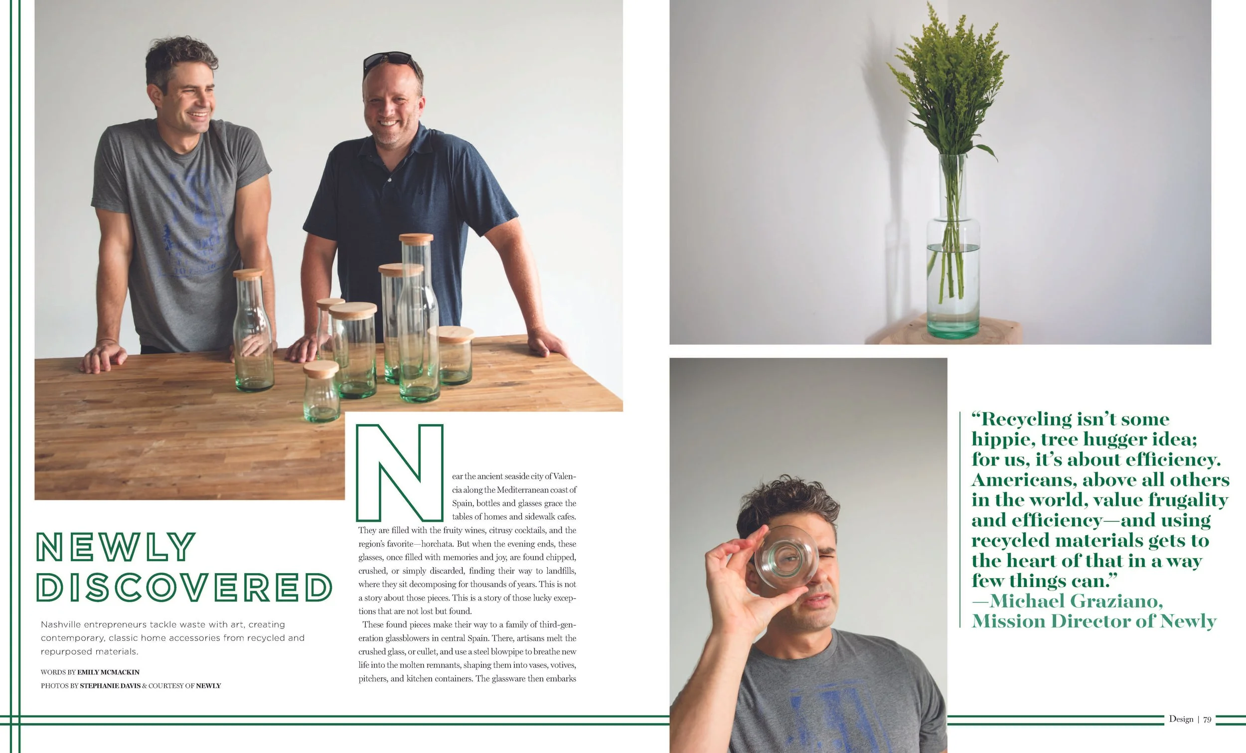 Two smiling men standing behind a wooden table with glass bottles, on the left side of the image. The right side shows a tall, narrow glass vase with green foliage against a plain wall.