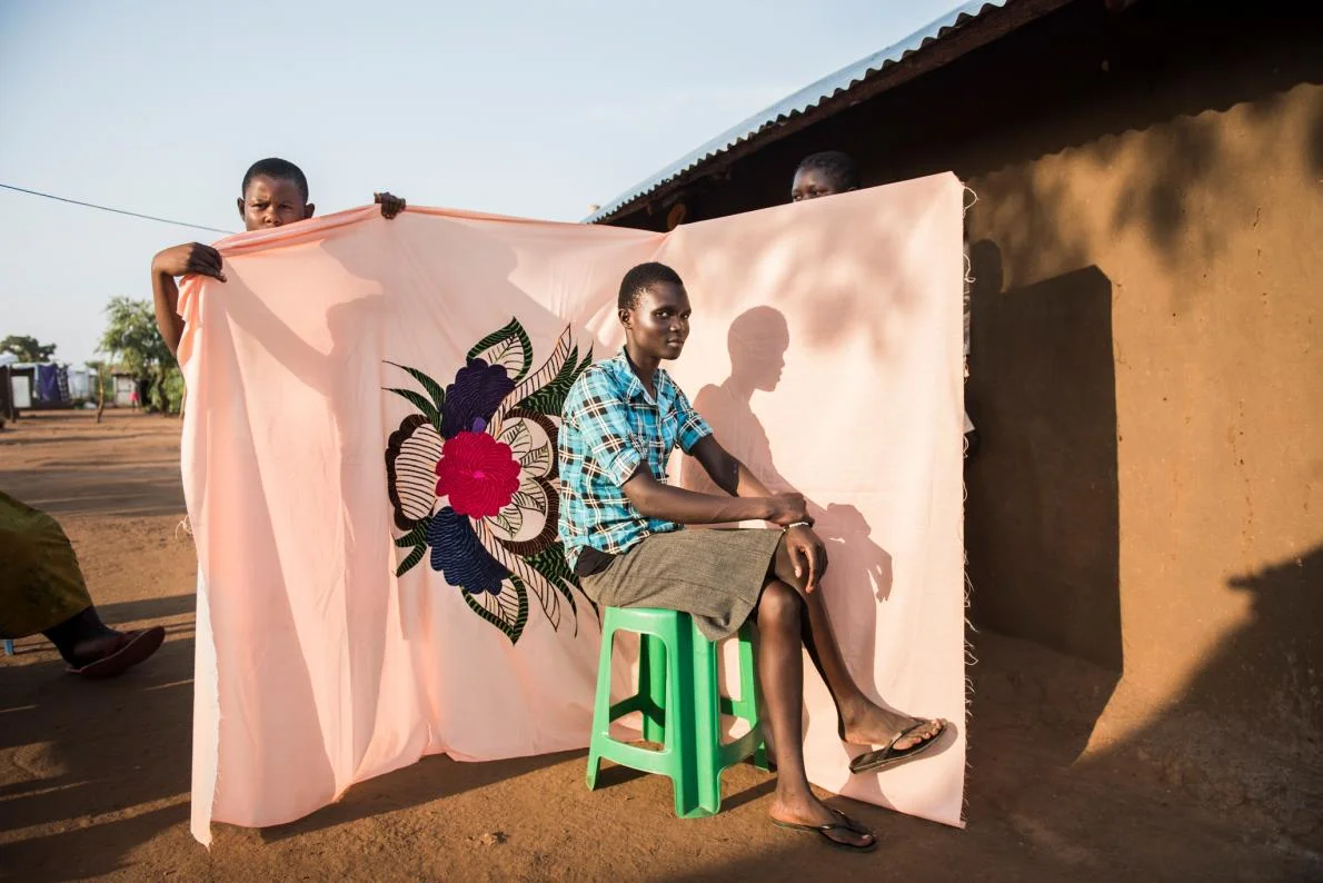 Irene Sonia poses in front of a milaya, or bedsheet—one of the few things her mother managed to bring when they fled South Sudan for Uganda. by NORA LOREK