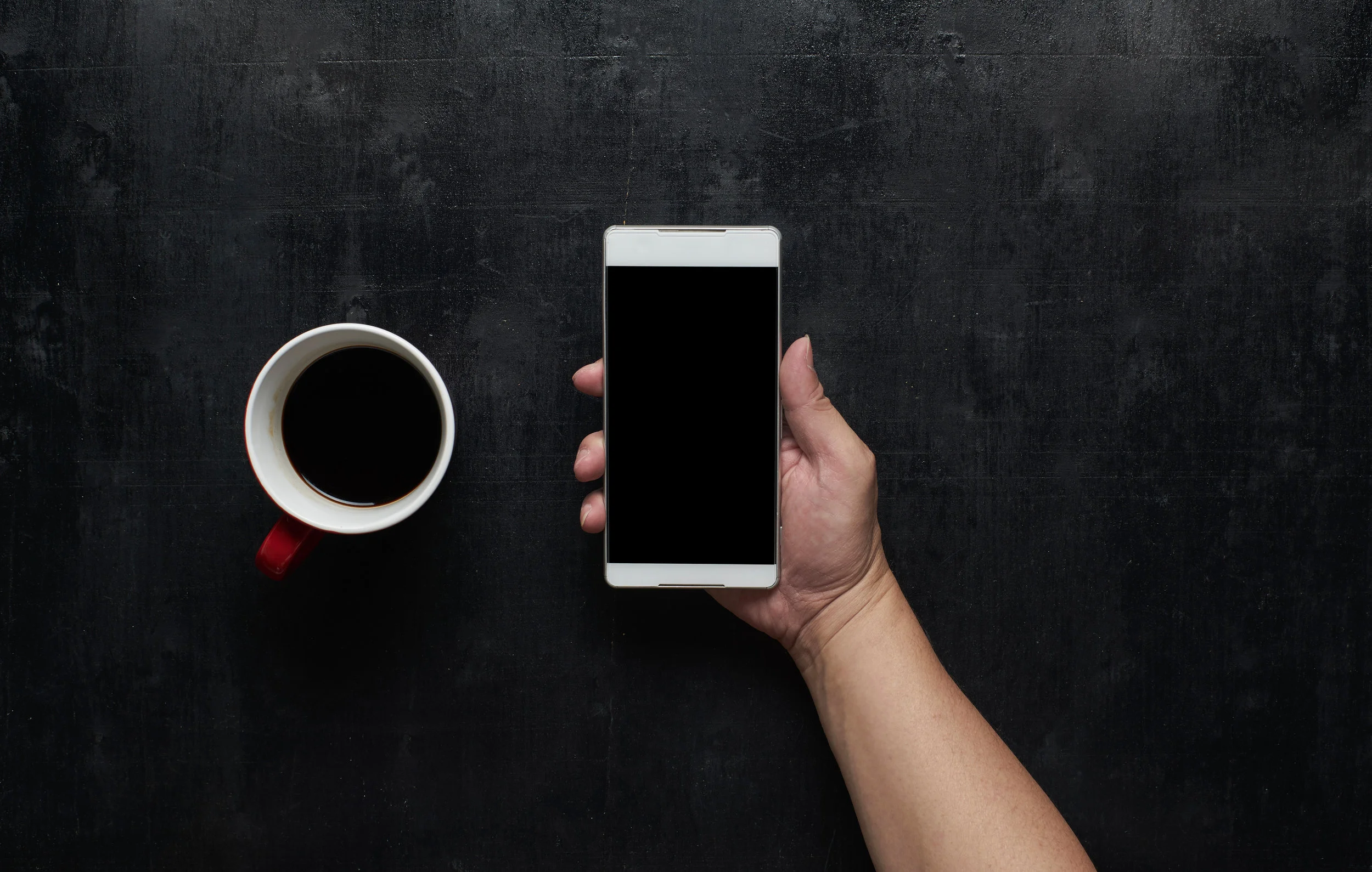 graphicstock-hand-holding-black-screen-smart-phone-with-cup-of-coffeewooden-black-office-desk-table-on-top-view_rOcgYoDeoe.jpg