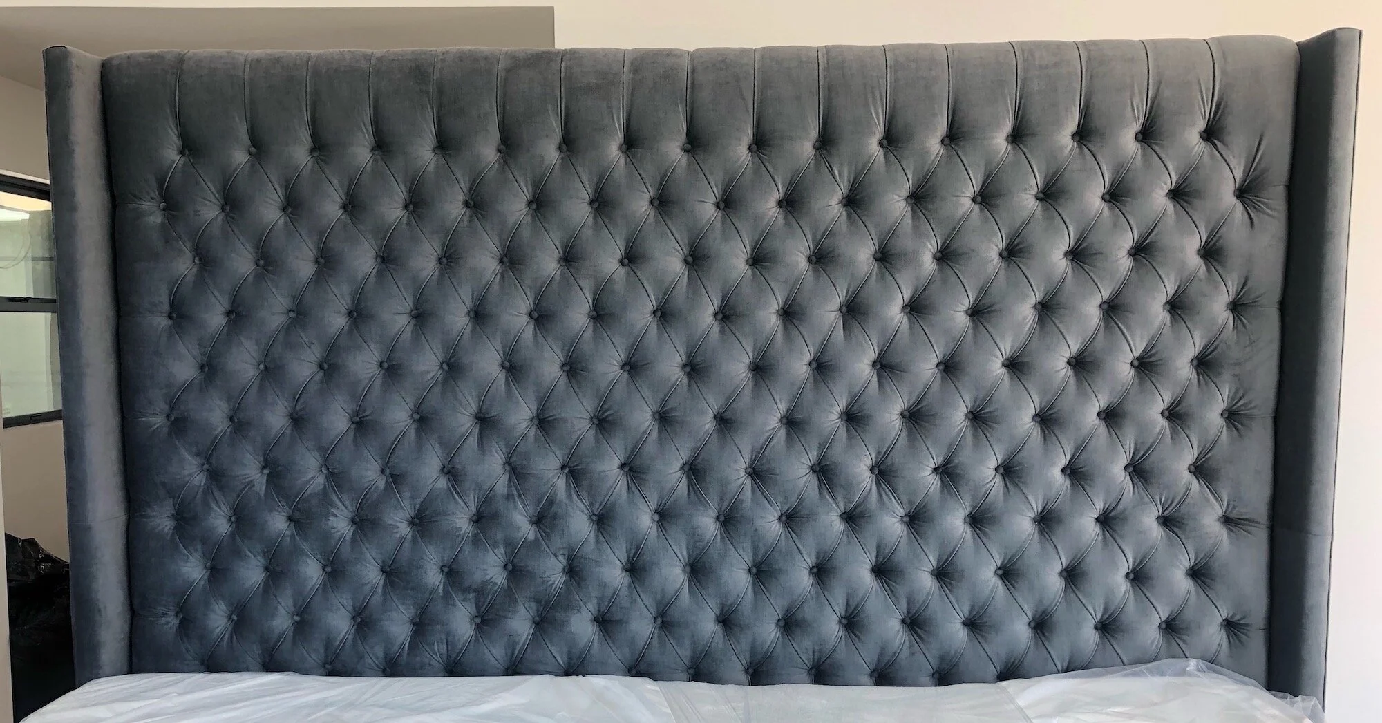Large bedroom headboard upholstered in dark gray velvet with a diamond-tufted, buttoned pattern