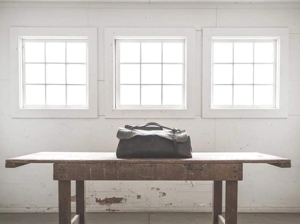 A solitary vintage leather bag displayed on a rustic table, representing unique objects of interest at Space Lab Vancouver.