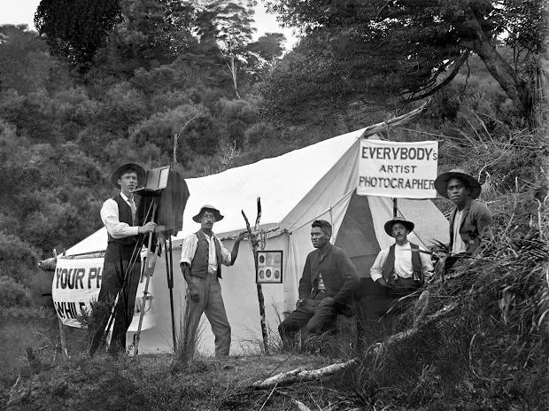 "While-you wait" photos. Photographers Enos Pegler (l) holding camera and tripod and Charlie Dawes (second from left). Photo / Dawes collection, Auckland Libraries