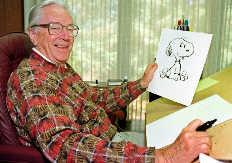 FILE - In this Feb. 12, 2000, file photo, cartoonist Charles Schulz displays a sketch of his beloved character “Snoopy” in his office in Santa Rosa, Calif. The home of “Peanuts” creator Schulz burned to the ground in the deadly California wildfires but his widow escaped, her stepson said Thursday, Oct. 12, 2017. Jean Schulz, 78, evacuated before flames engulfed her hillside home Monday and is staying with a daughter, Monte Schulz said. (AP Photo/Ben Margot, File)