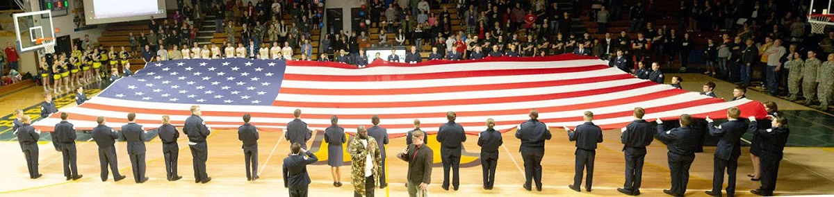 Members of Henley High School’s 931st Air Force Junior ROTC unfurl and hold a 30-by-60 foot American flag while Henley choir teacher Chris Benjamin and Henley student Zach Marchessault sing a duet of the national anthem. (Photo by Carlos Becerra)