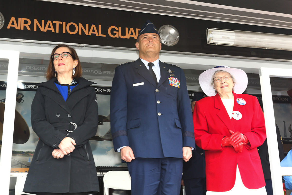  Oregon Governor Kate Brown (left) along with Maj. Gen. Mike Stencel, Adjutant General, Oregon (center) and official honoree Joy Beebe, a WWII war bride, (right) stand for a howitzer salute by the "Governor's Own" Bravo Battery, 2-218th Field Artille