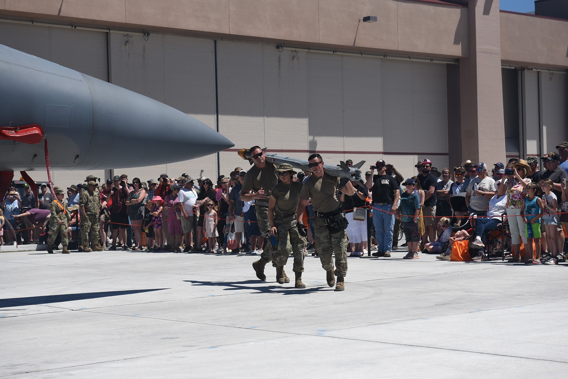  U.S. Air Force Master Sgt. Timothy Saindon, Tech. Sgt. Ashley Vela, and Staff Sgt. Philip Snoozy, all of the 173rd Fighter Wing weapons shop, demonstrate weapons-loading skills for assembled spectators at the Sentry Eagle 2022 open house at Kingsley